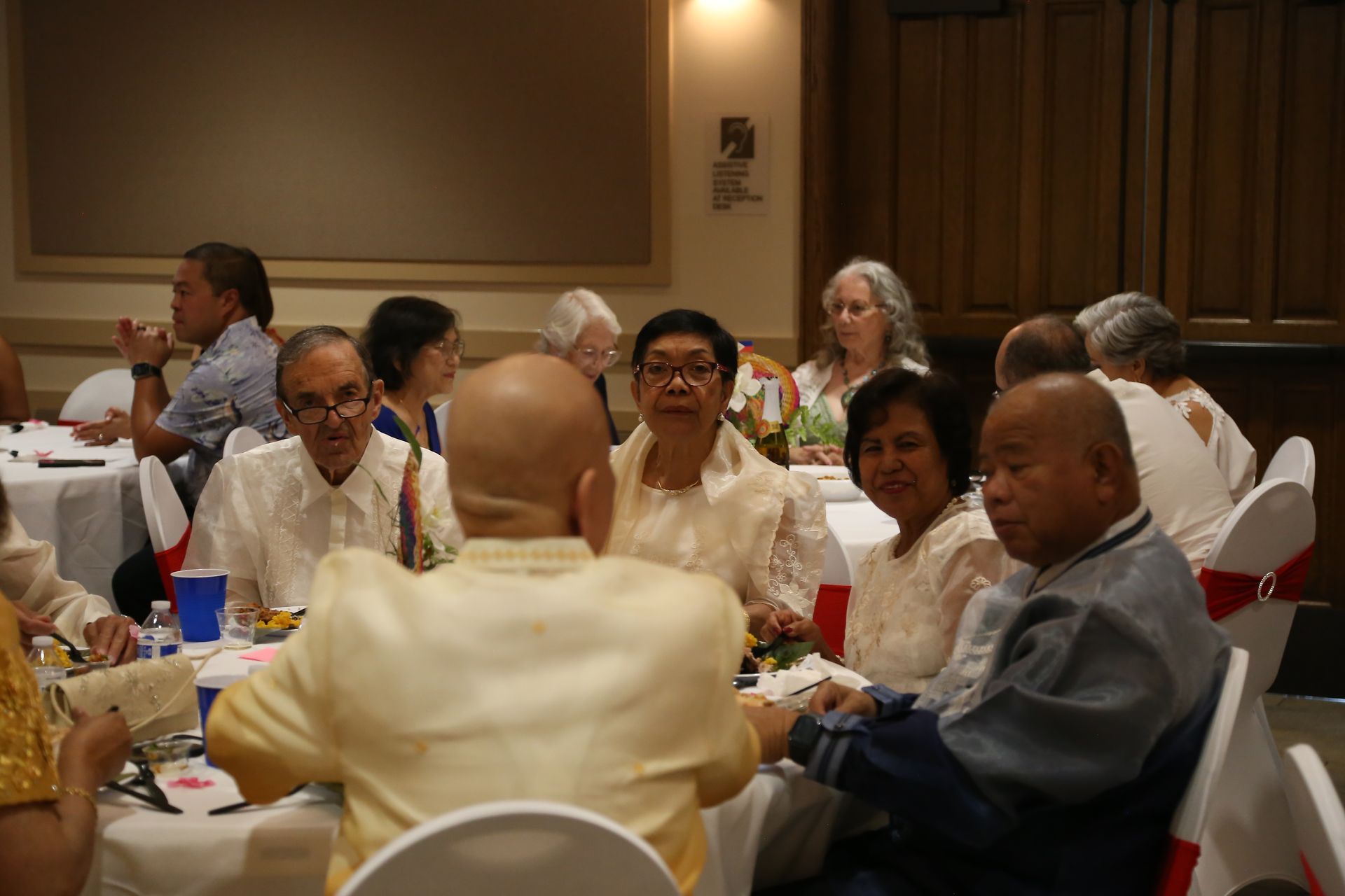 Guests seated at round tables chatting in a banquet hall with white tablecloths and warm lighting