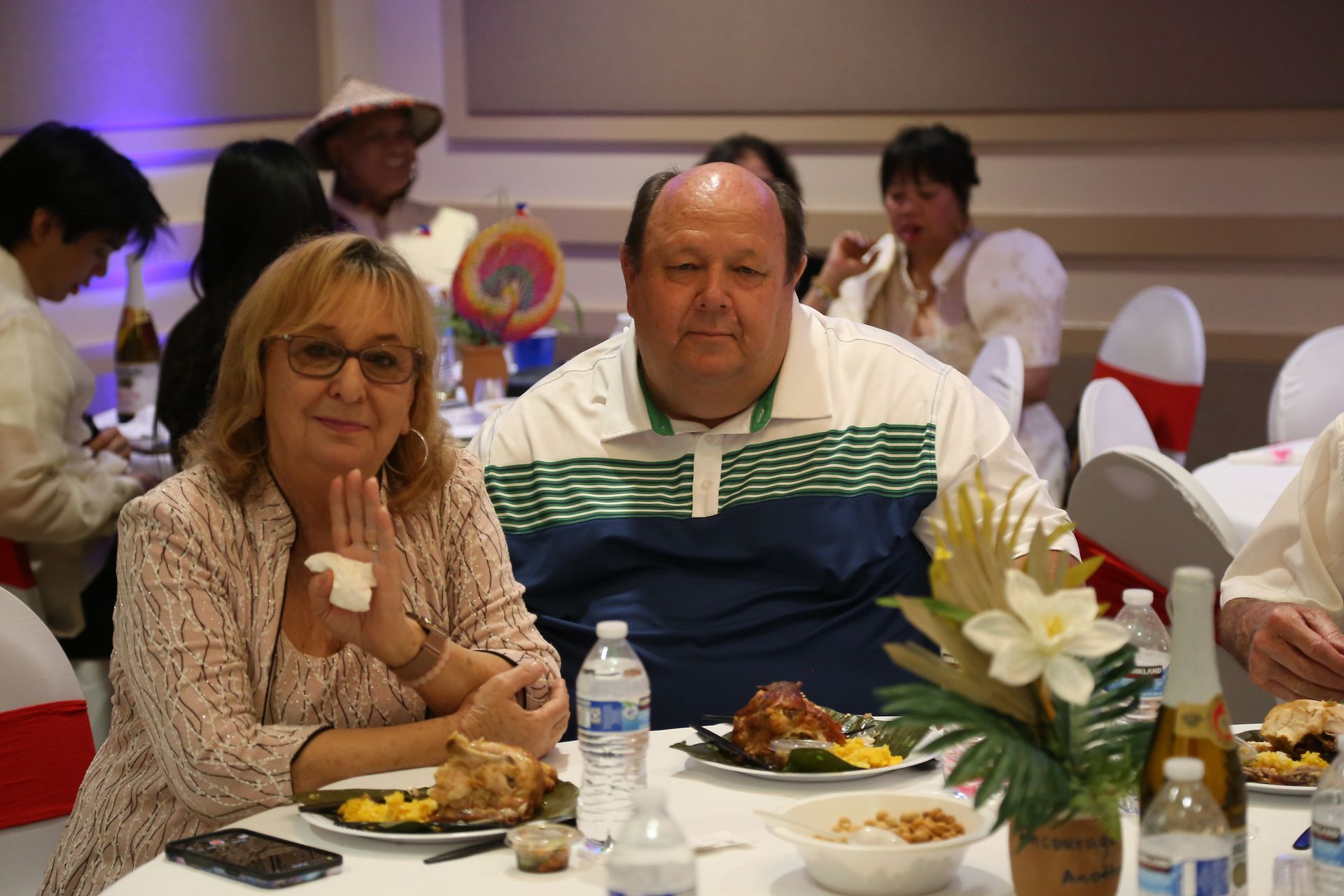 Two people seated at a banquet table with plates of food and a floral centerpiece