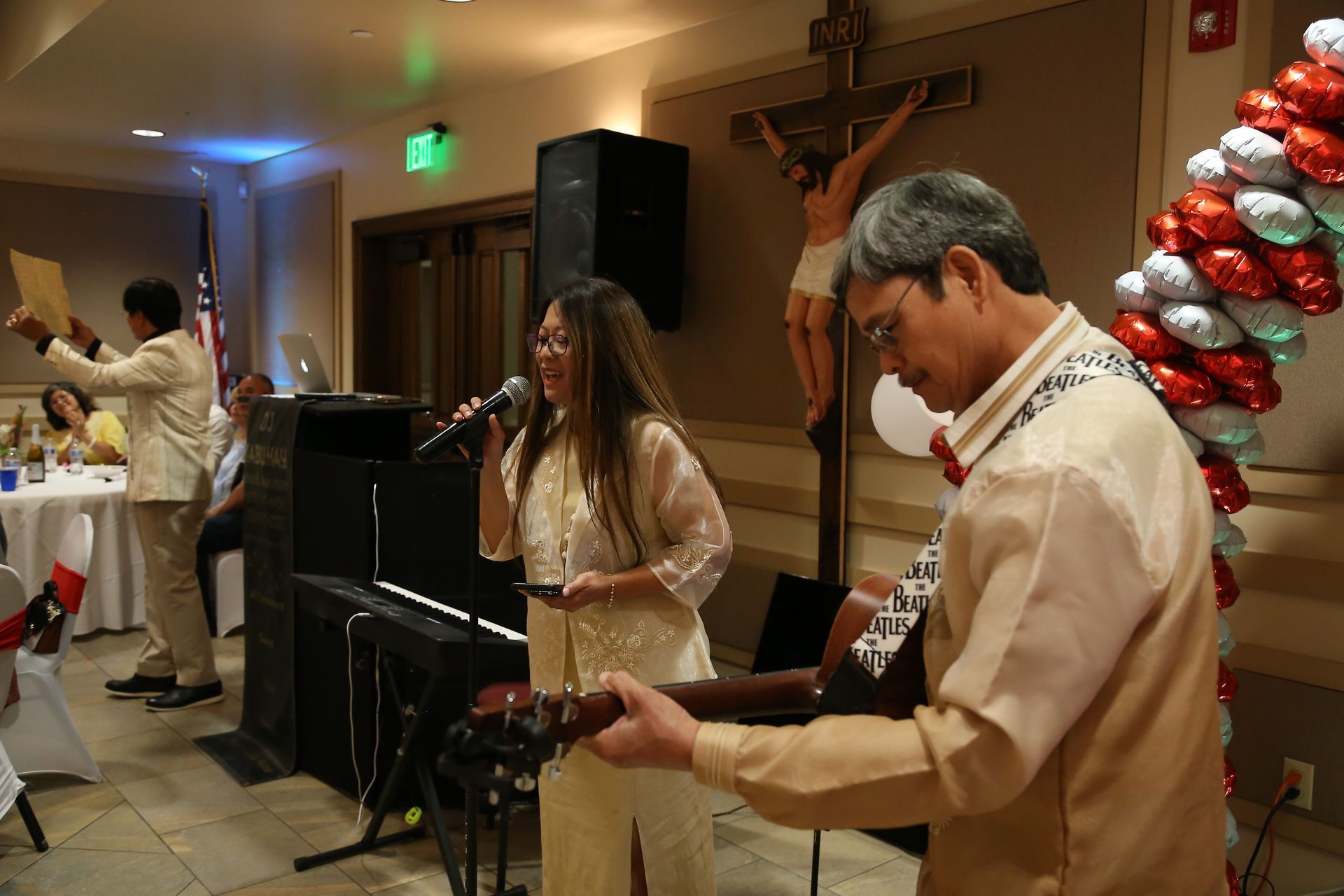 Live band performing indoors with singer, guitarist, and festive red balloon decorations in the background