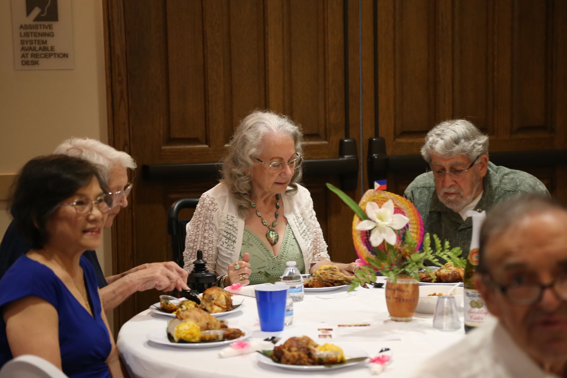 People seated at a dining table with food and drinks in a wood-paneled room