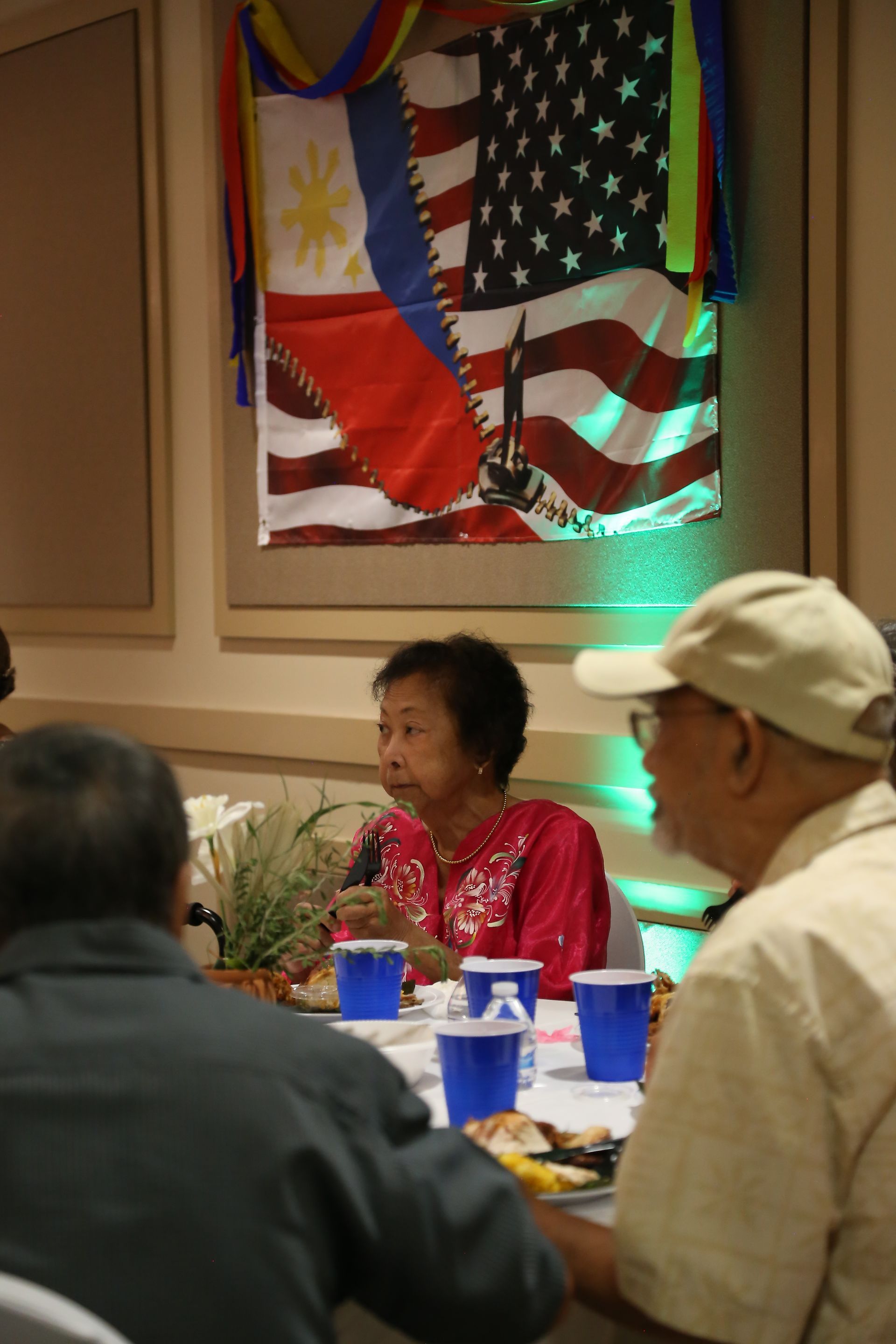 People seated at a table in a banquet room beneath a colorful flag display