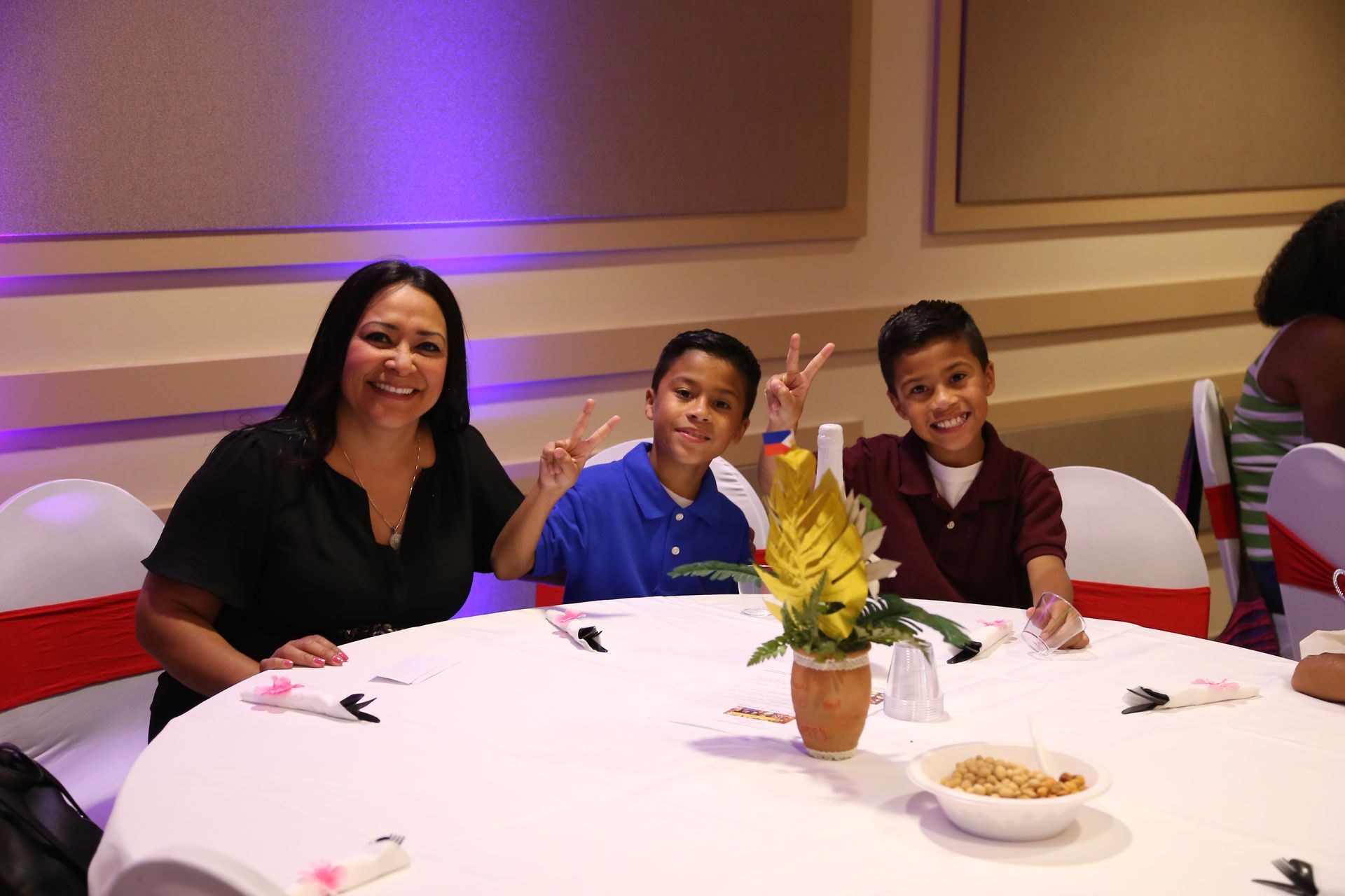 Three people smiling at a banquet table with a flower centerpiece in a decorated hall