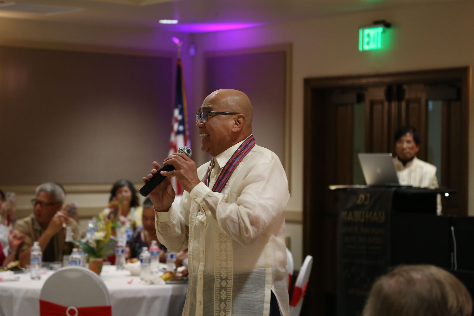 Man speaking into a microphone at a banquet, with an audience seated at tables nearby