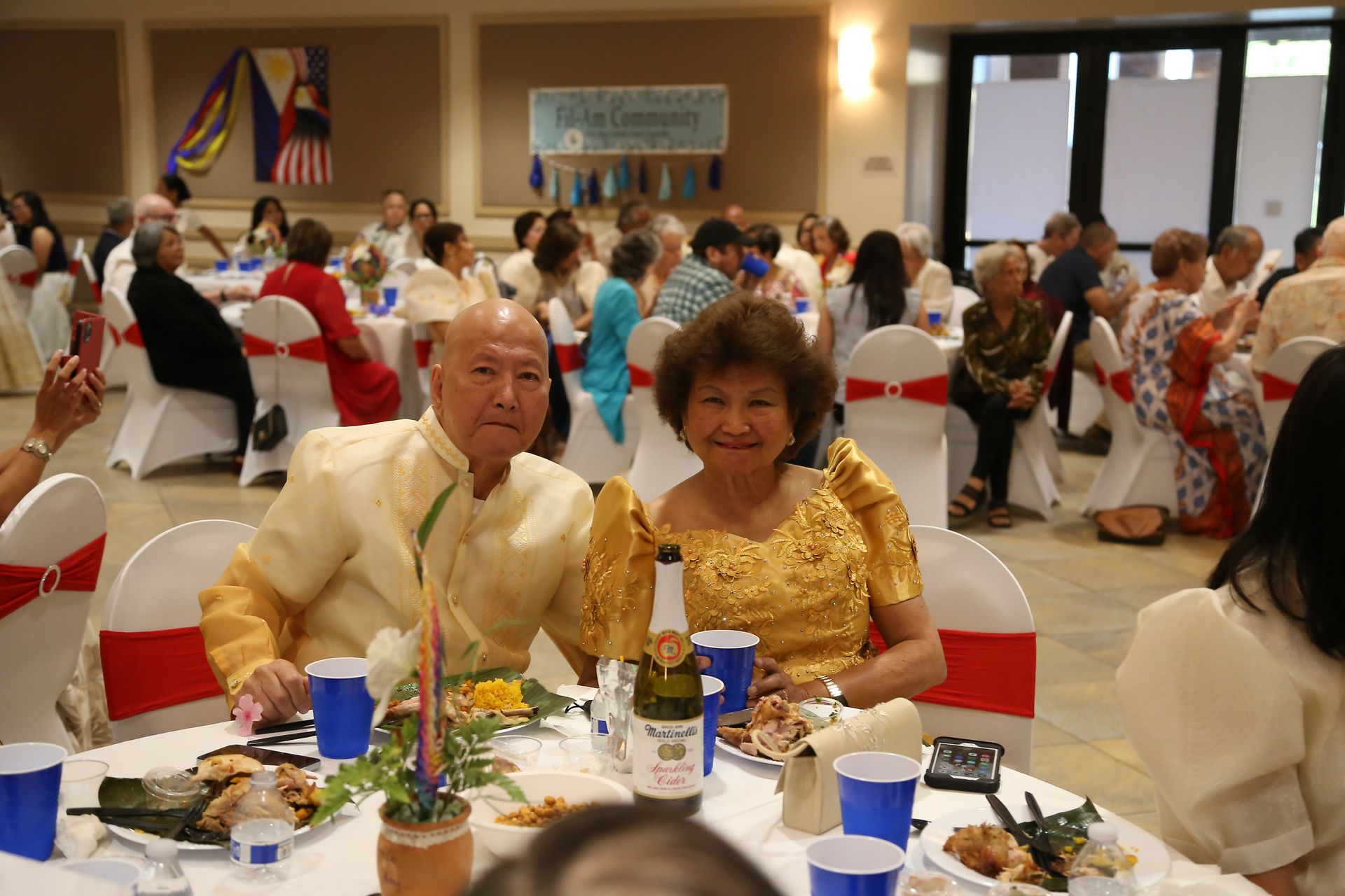 Banquet guests seated at round tables in a decorated hall, with a smiling couple in the foreground
