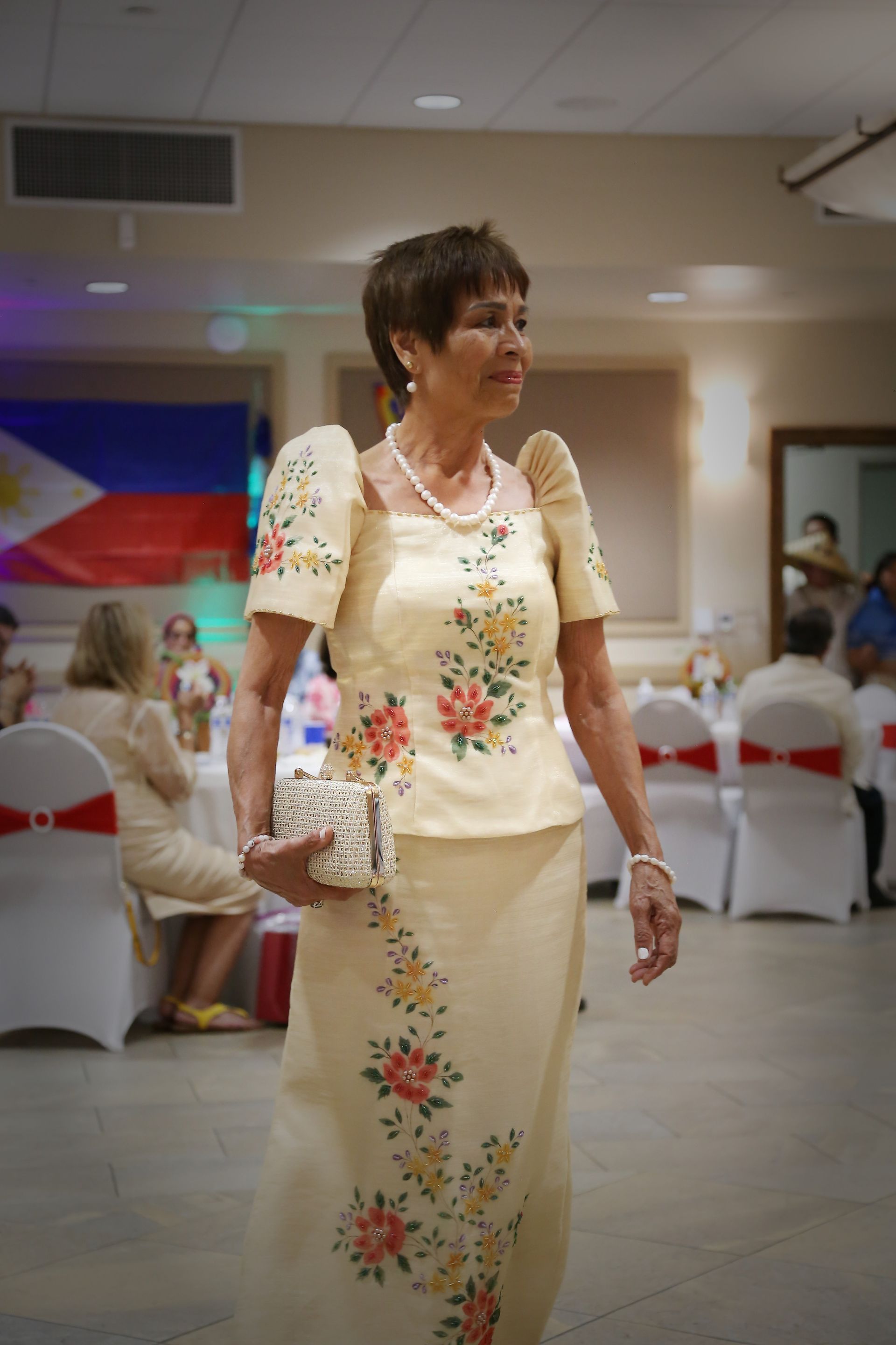 Woman in cream floral dress standing in a banquet hall with decorated tables and chairs