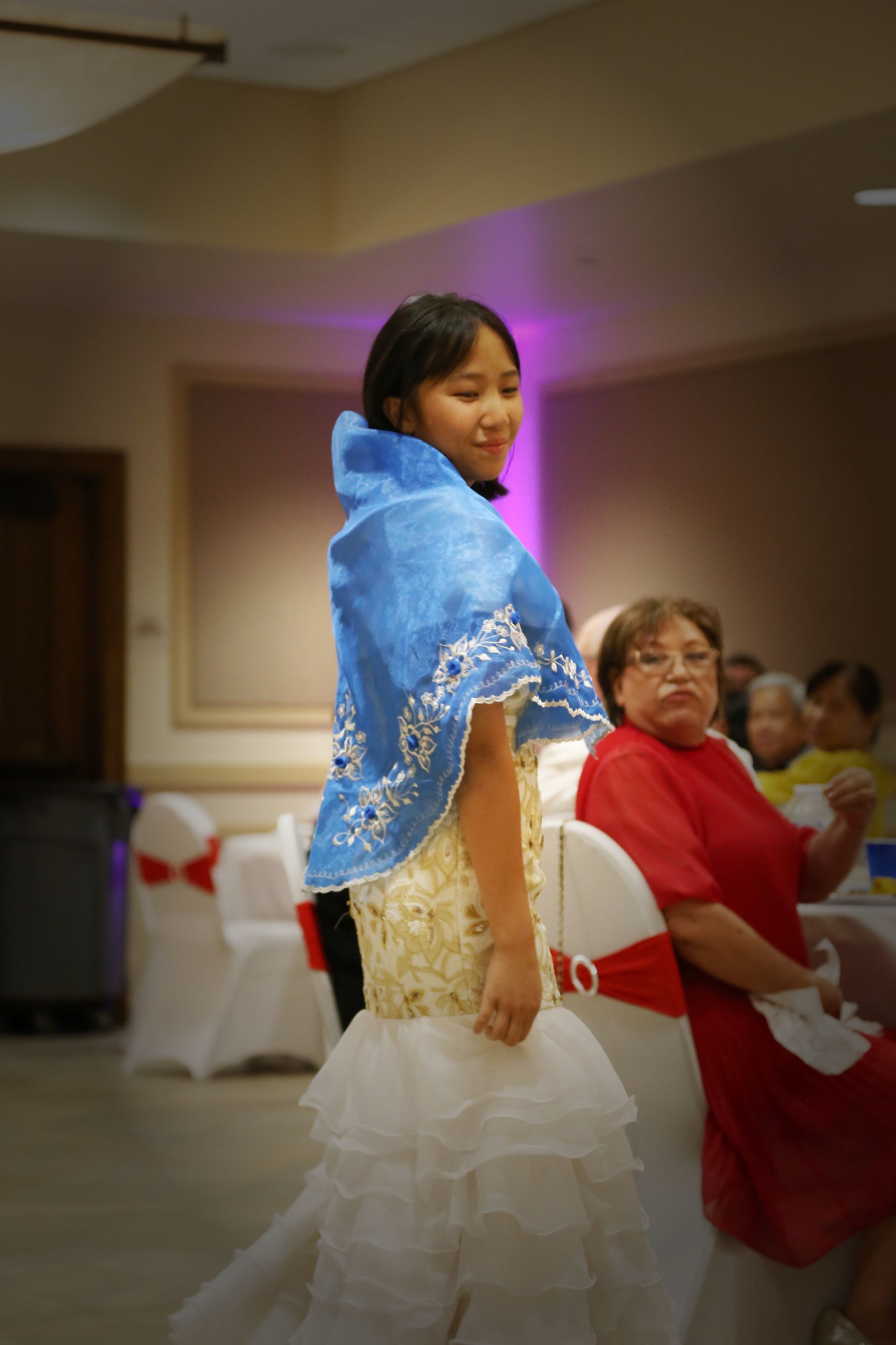 Woman in blue shawl and white dress dancing at a decorated indoor event