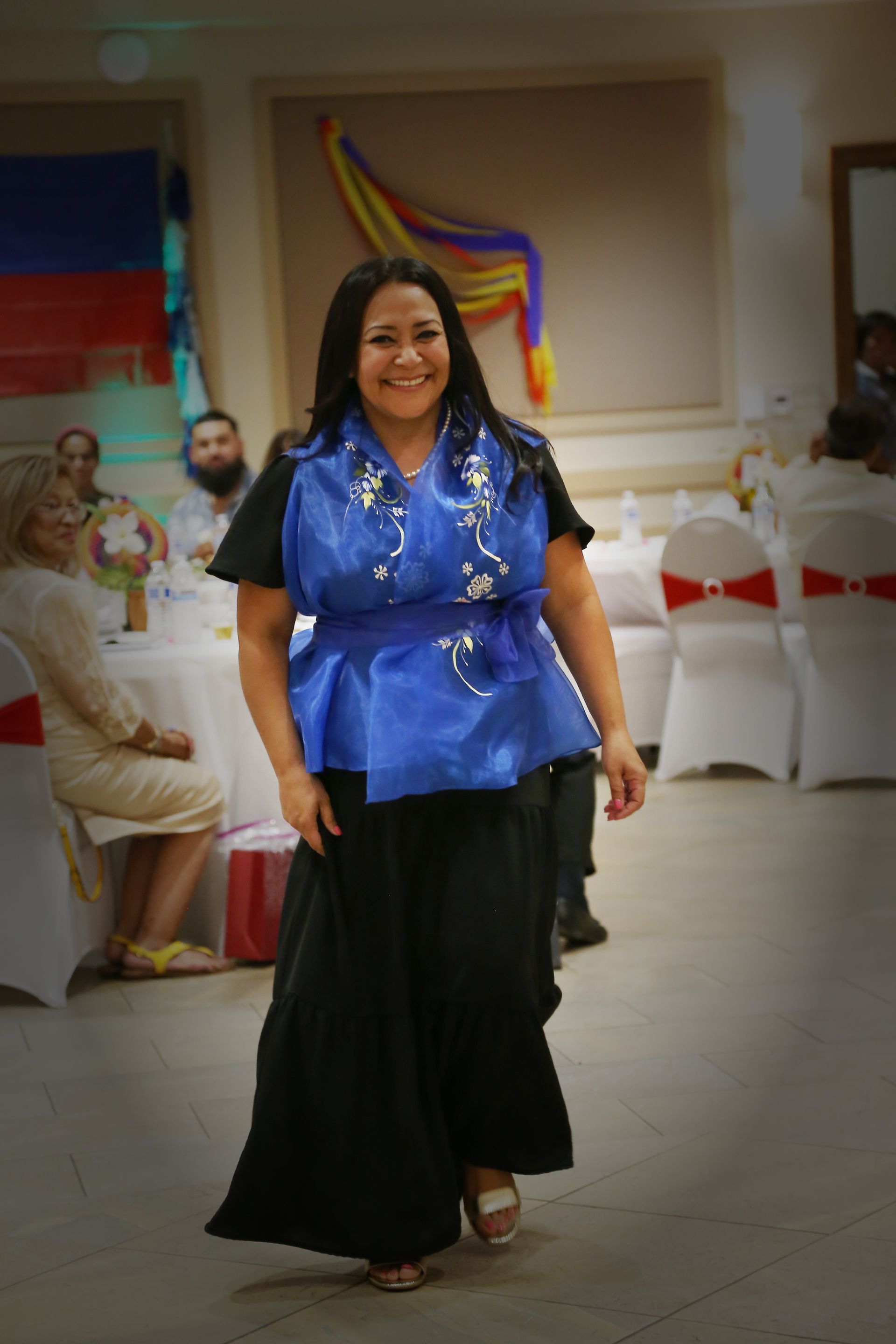 Woman in a blue blouse and black skirt walking indoors at a festive event