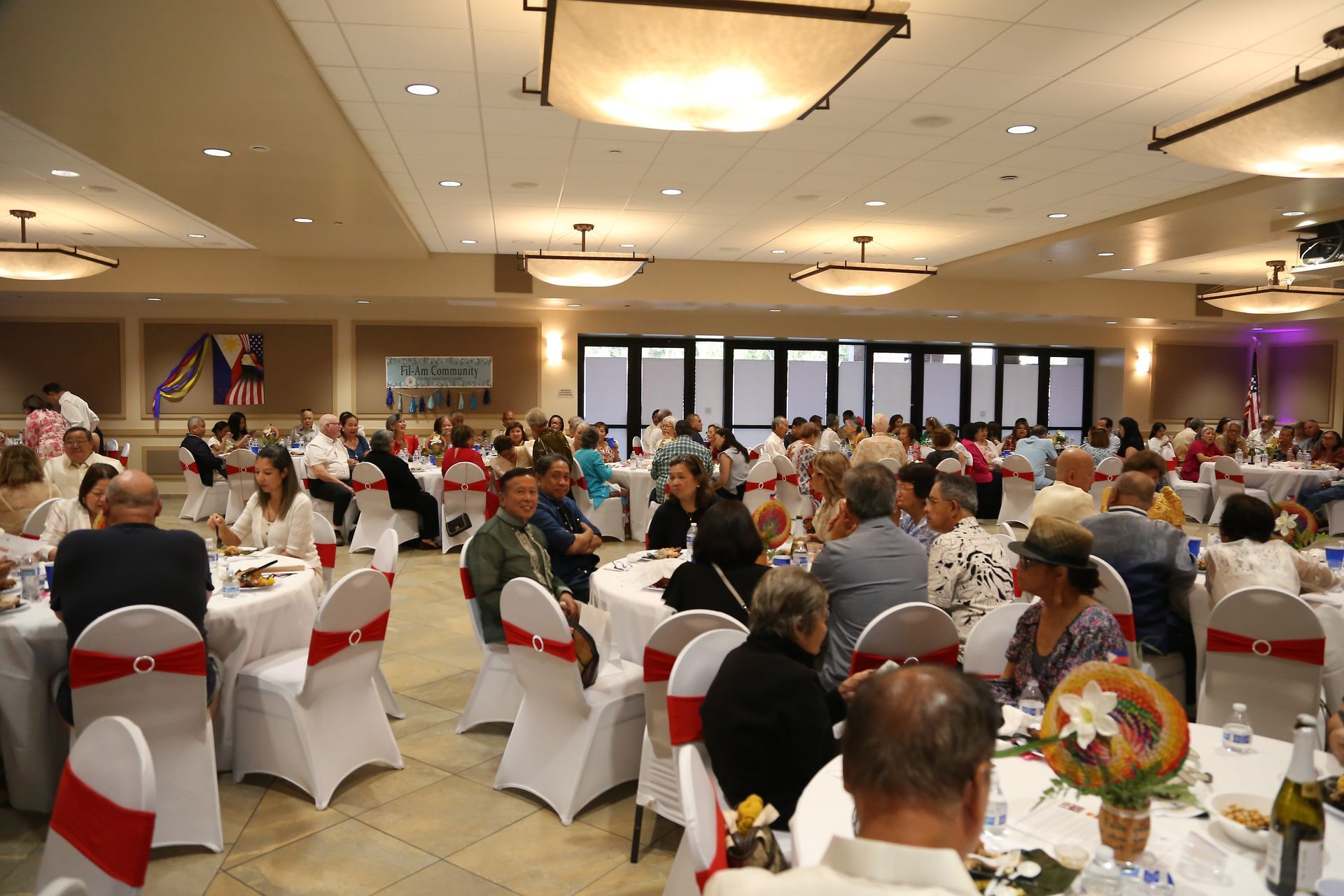 Banquet hall with guests seated at round tables, white chair covers, and a stage in the background