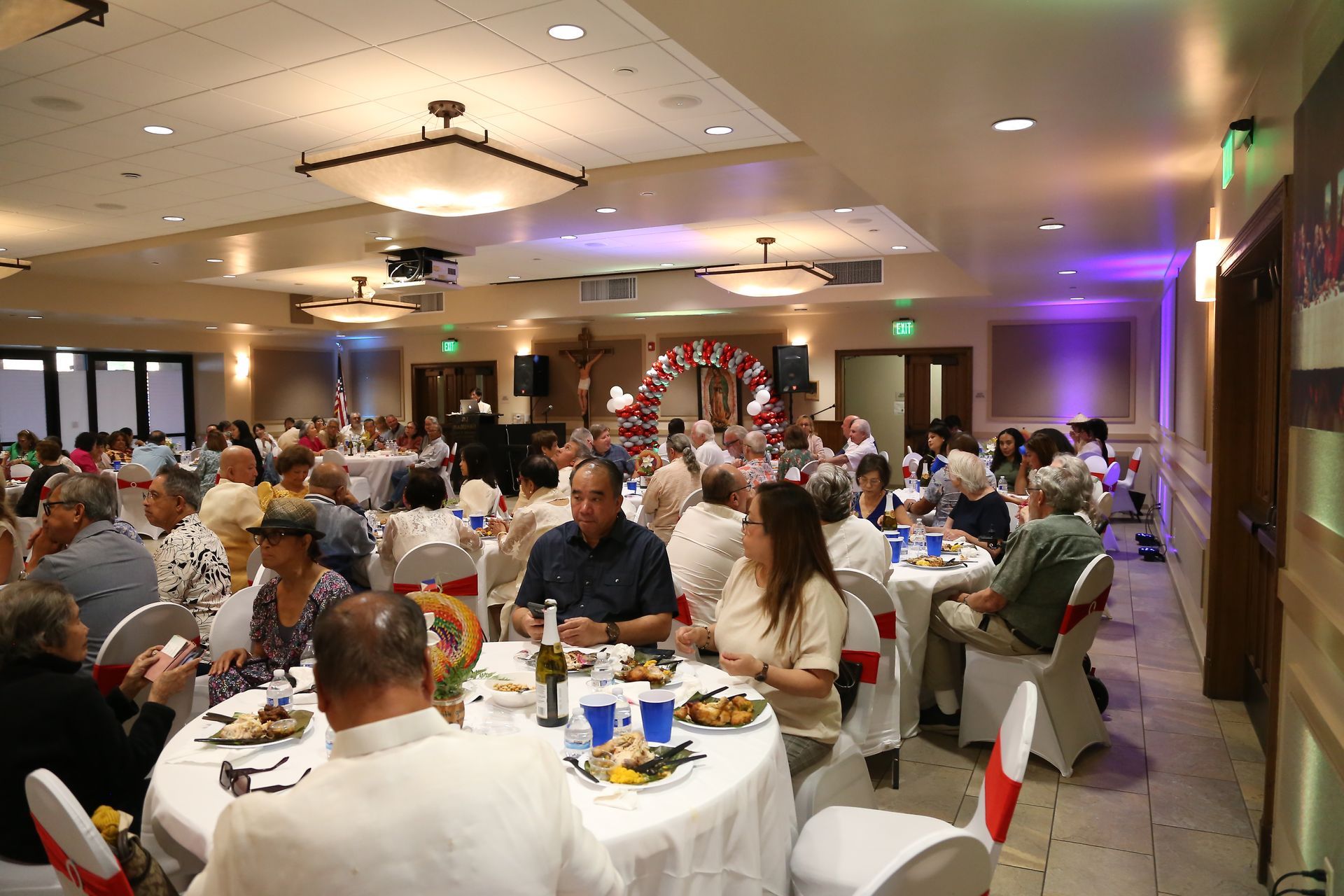Banquet hall filled with guests seated at round tables, with soft lighting and a decorated backdrop.
