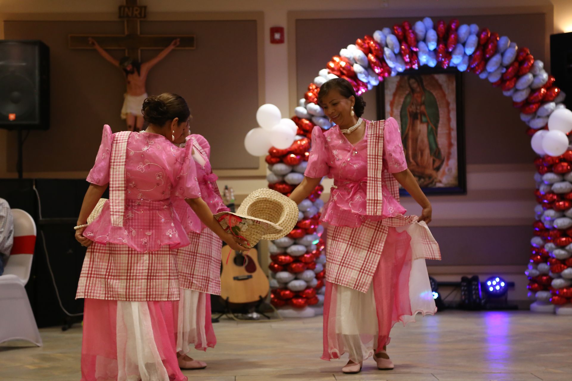 Two dancers in pink traditional outfits perform on a decorated stage.