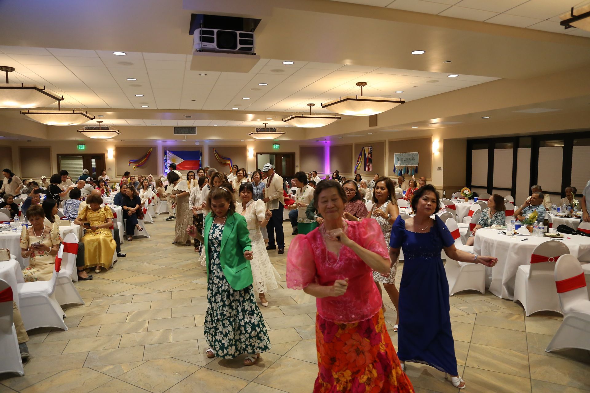 People dancing at a banquet hall with round tables and pink-purple lighting