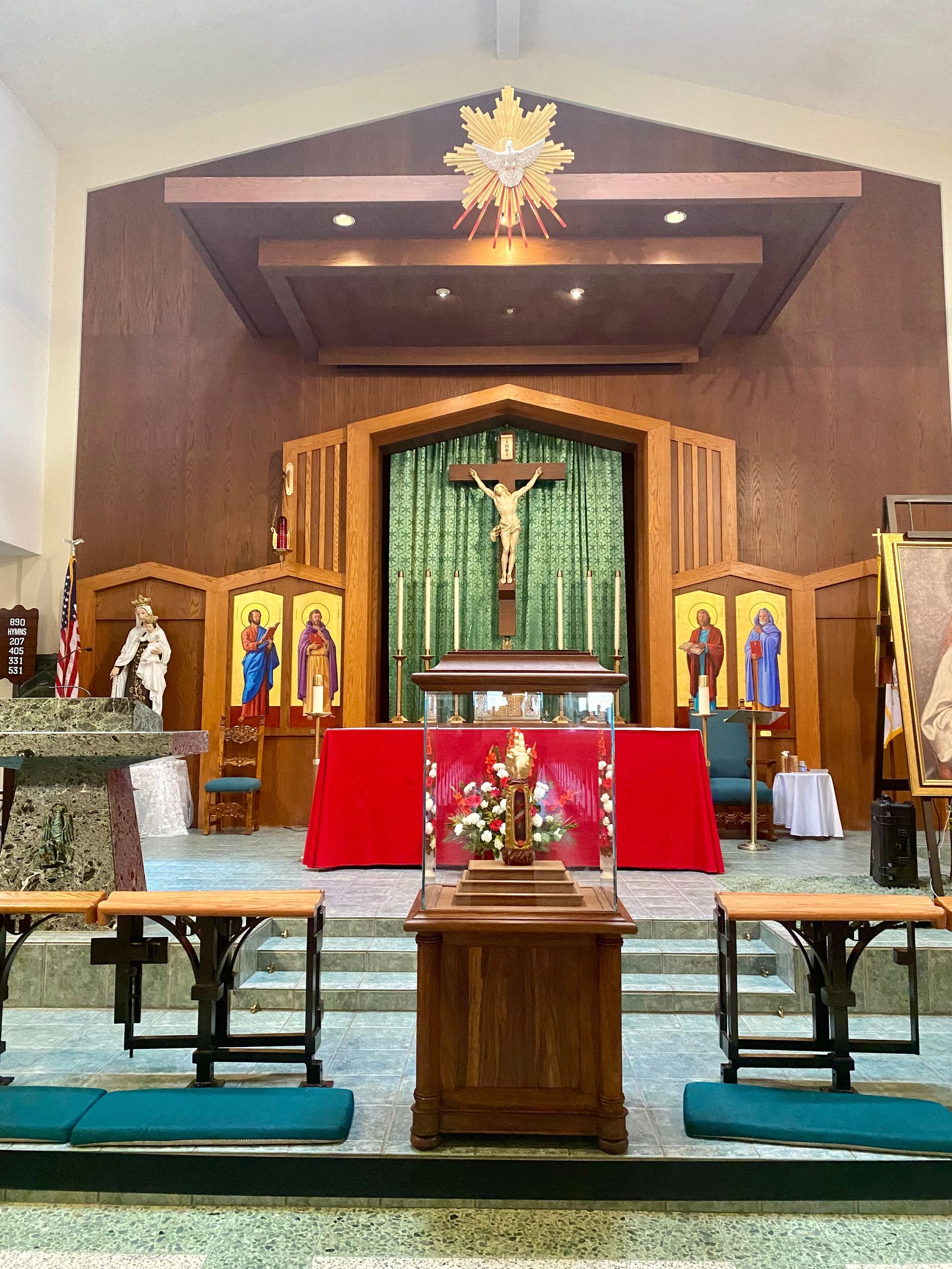 Catholic church altar with crucifix, green drapery, red altar cloth, and candles in a wood-paneled sanctuary