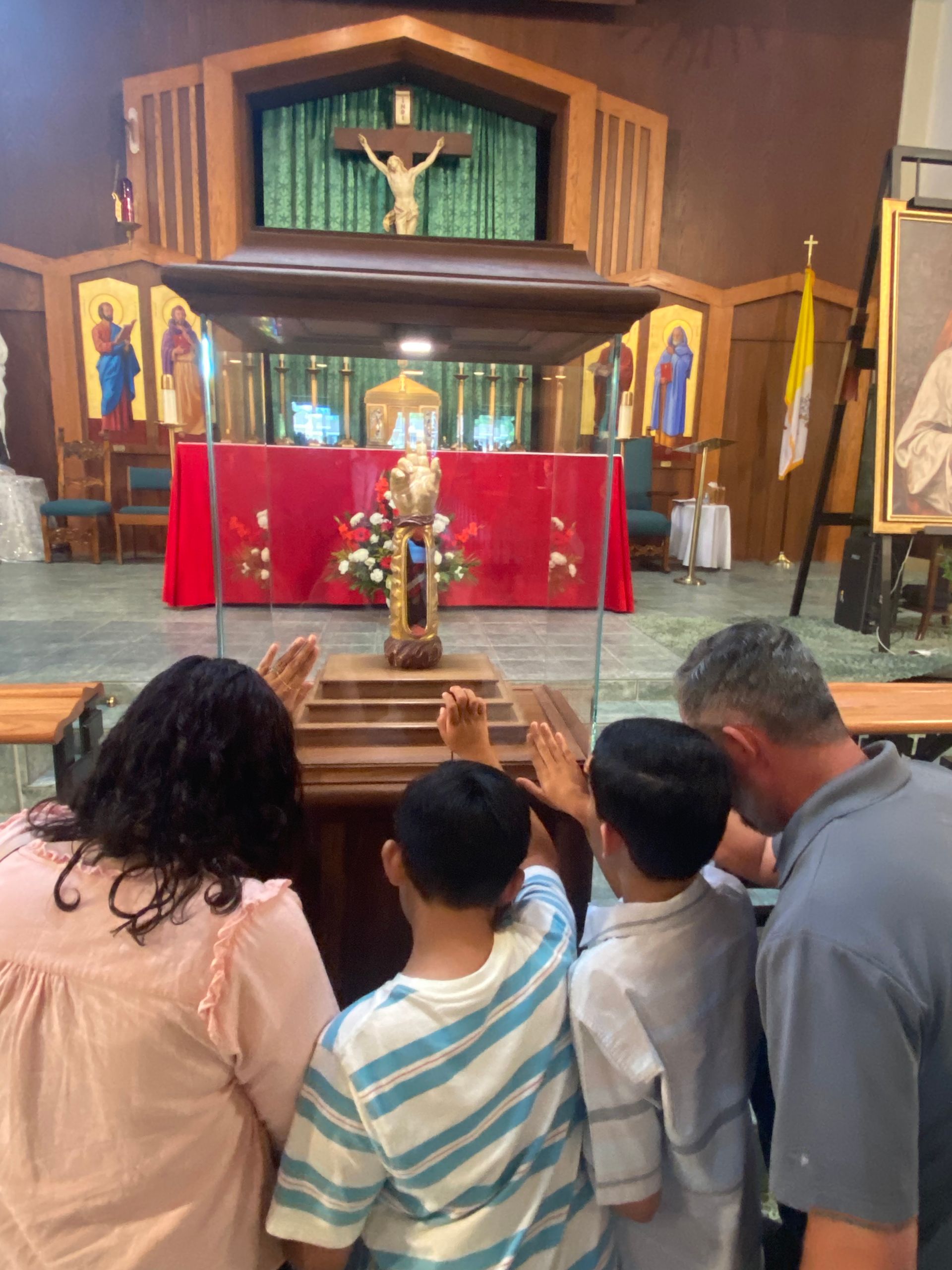 People kneel in a church, facing the altar and crucifix draped in red cloth.