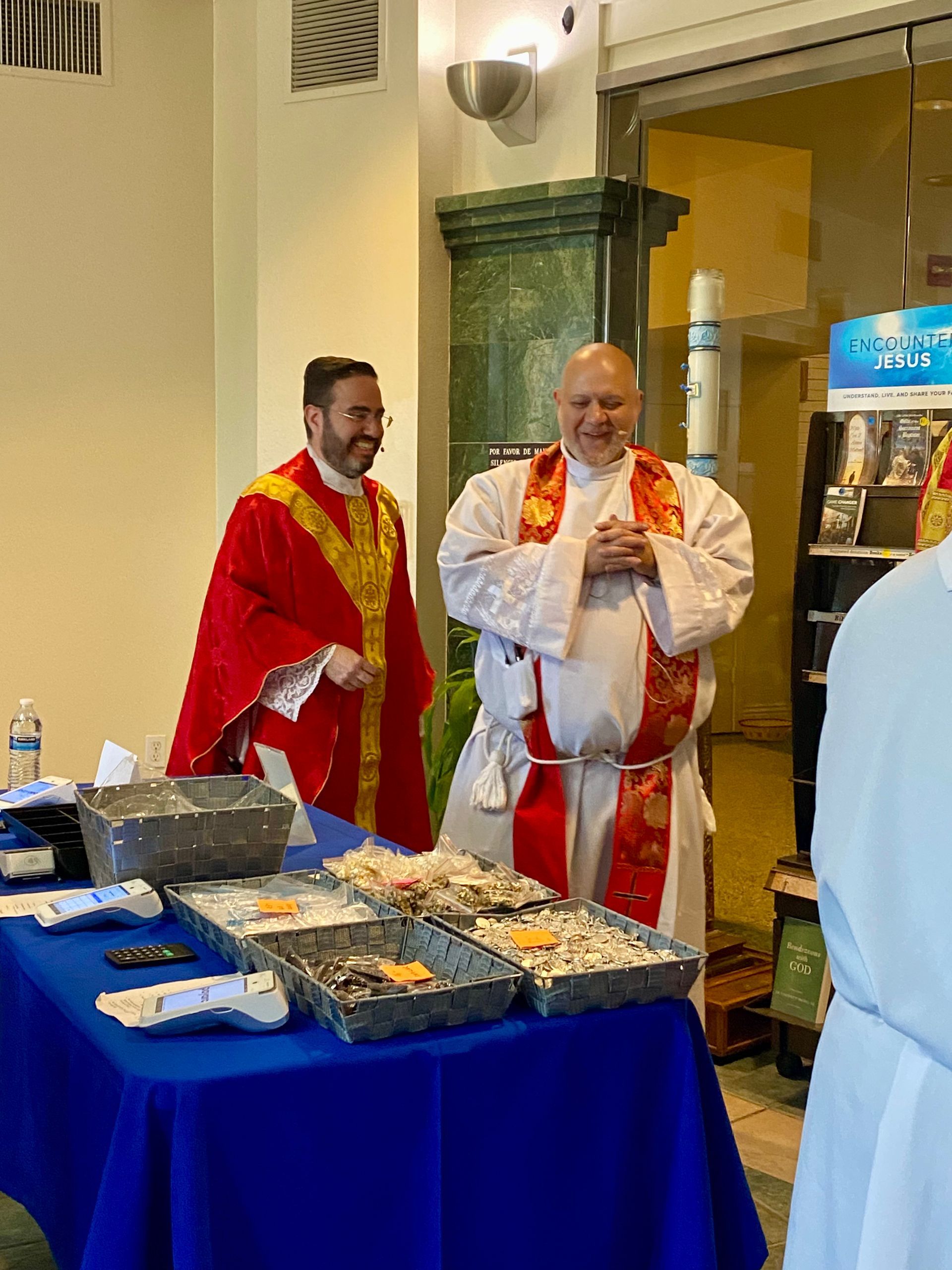 Two men in red-and-white robes stand beside a buffet table in a warmly lit hall