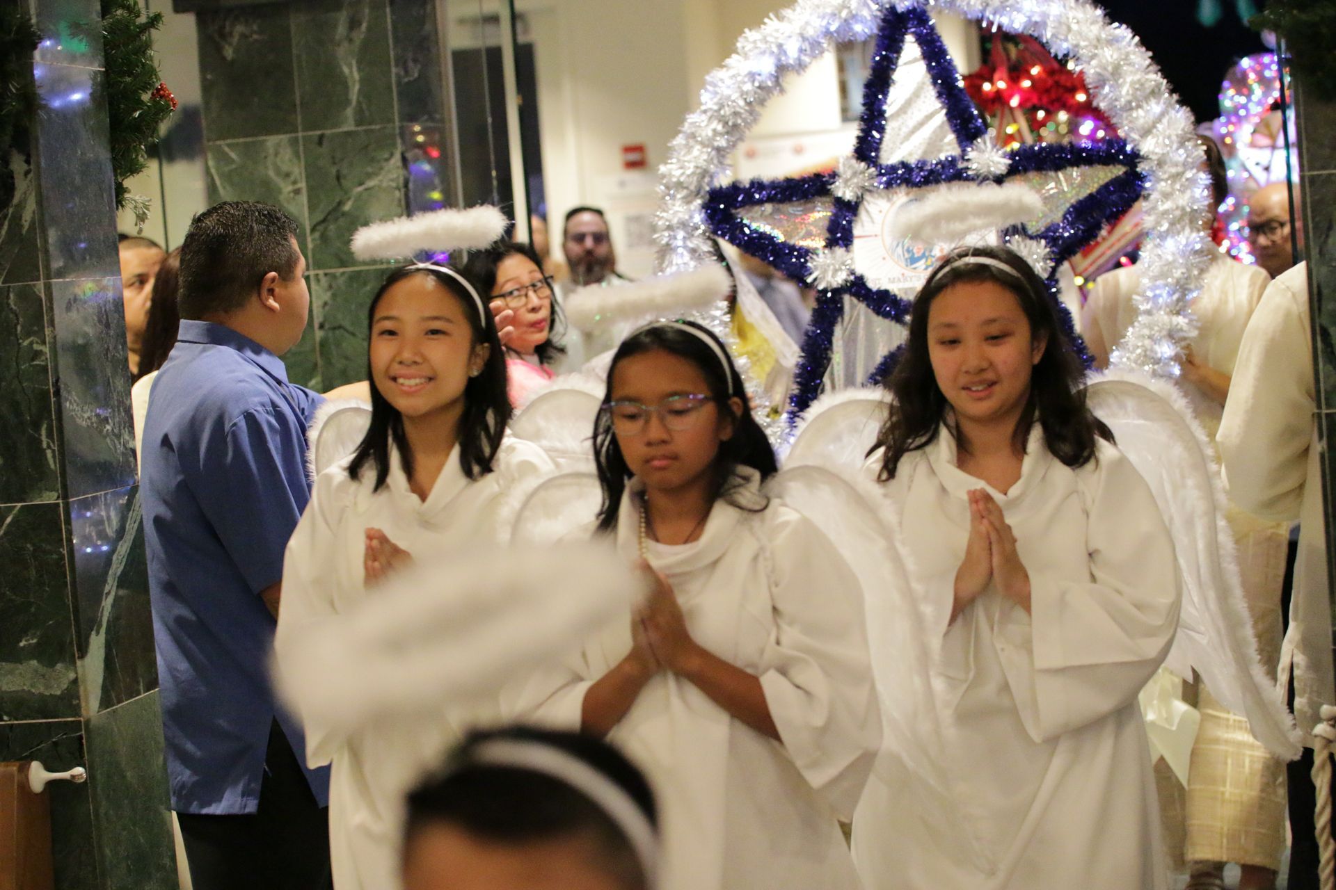 Three people in white robes walking in a festive procession with a large illuminated star backdrop