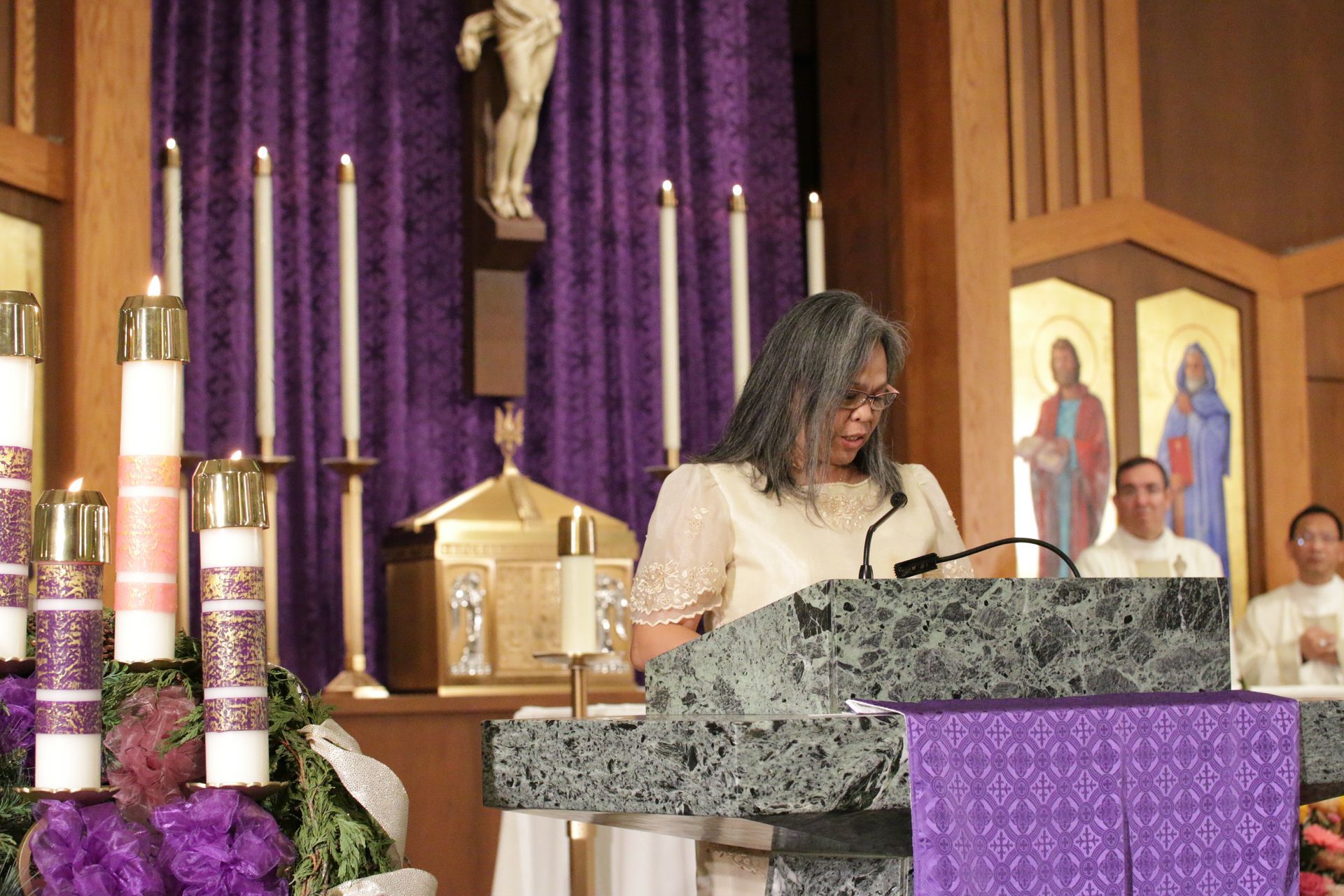 Woman speaking at a church lectern with purple altar cloths and candles in the background