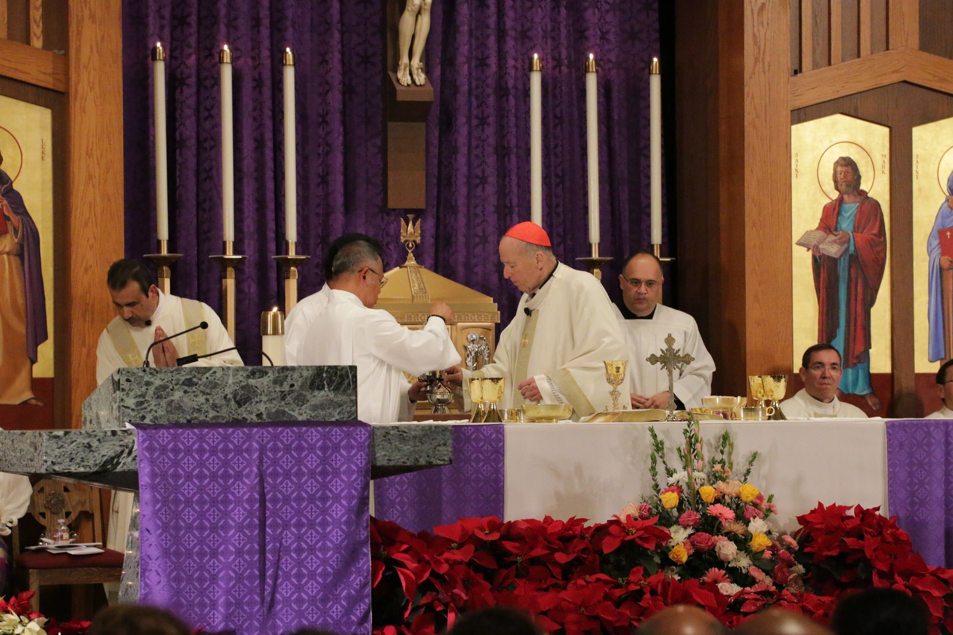 Priests celebrating Mass at a church altar with purple drapery and floral arrangements