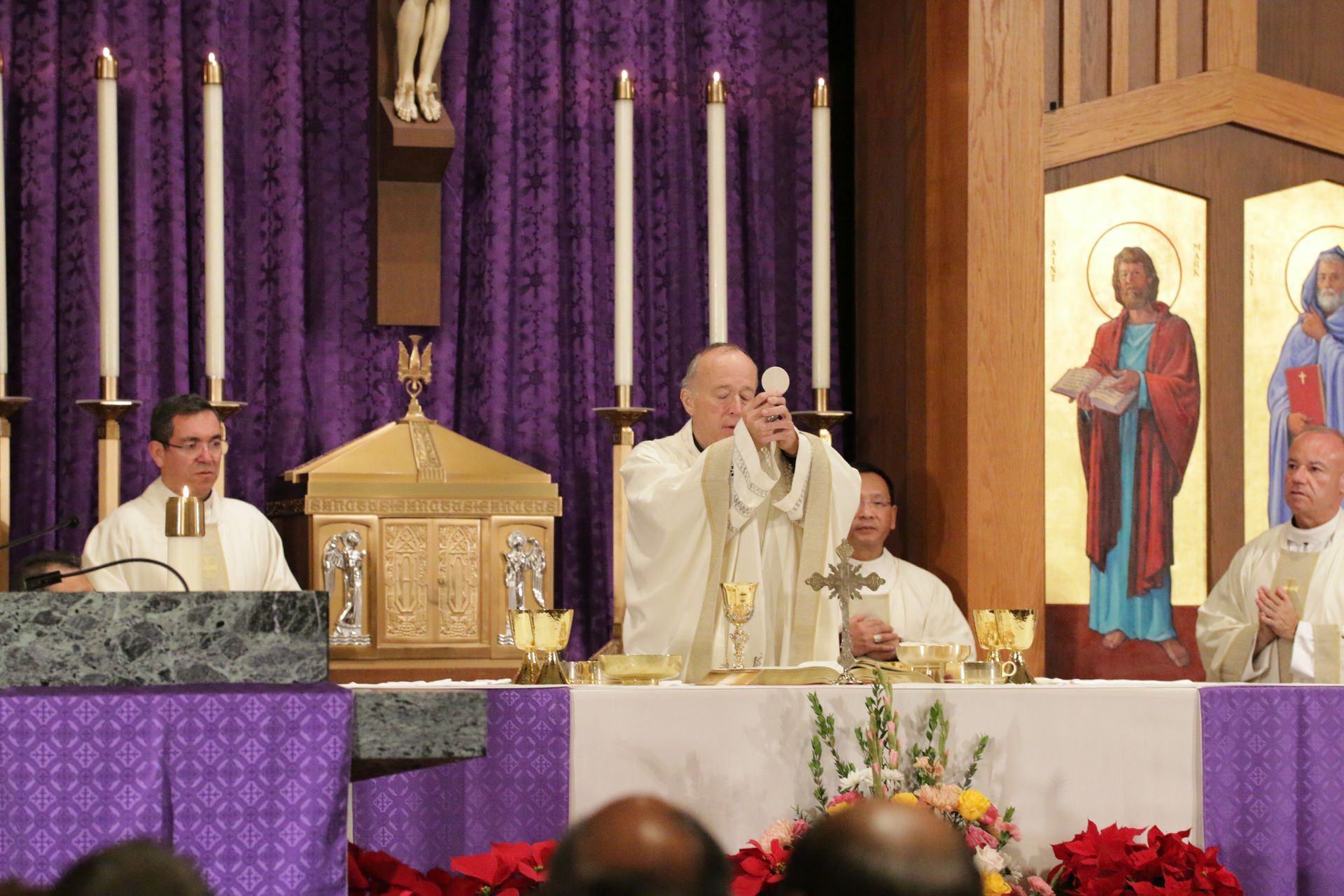 Priest celebrating Mass at altar with purple drapery and candles in a church sanctuary