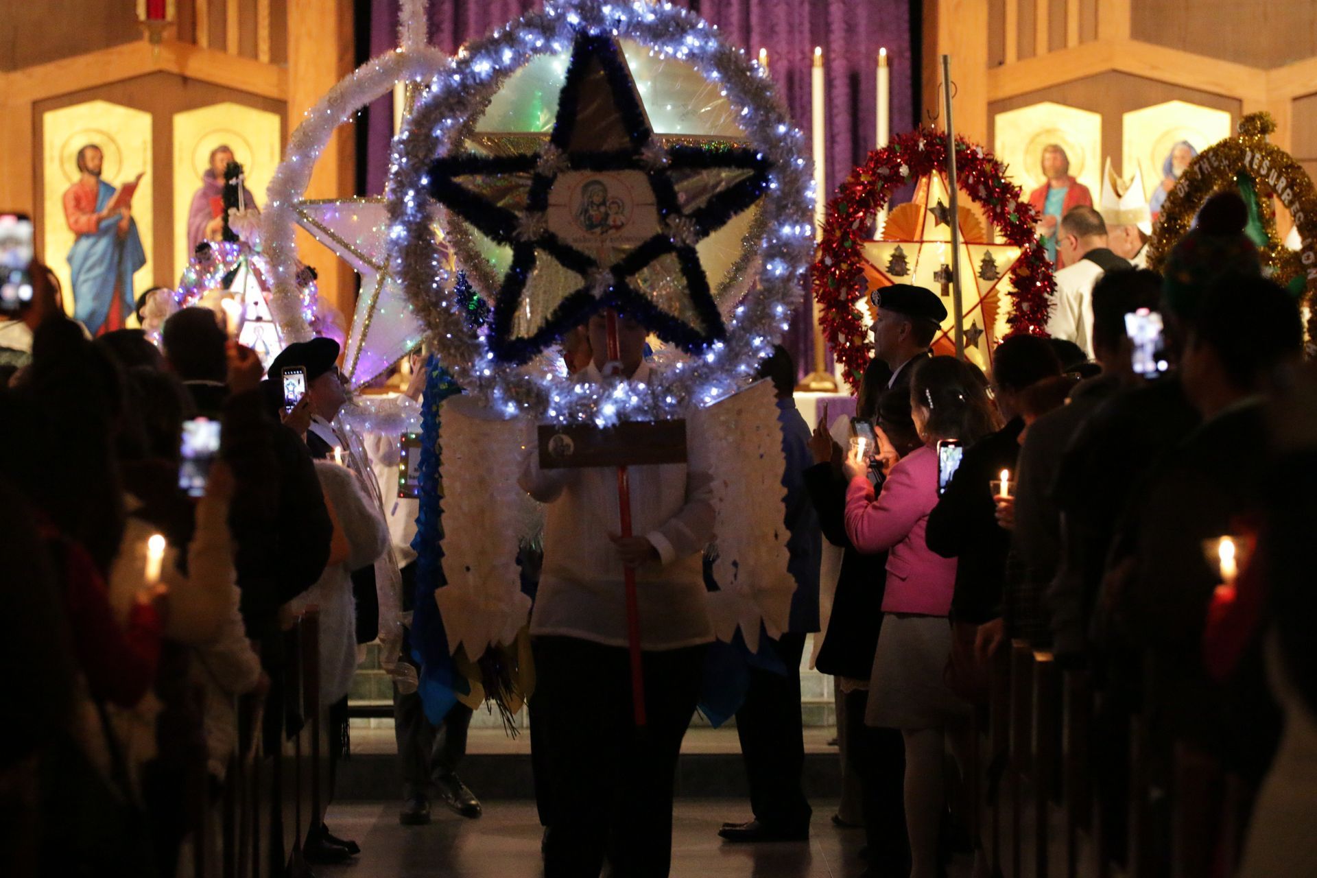 People in a dim church procession carrying glowing star lanterns and candles at night