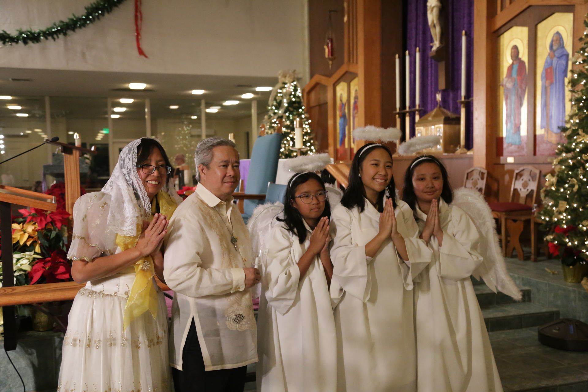Five people in white robes stand inside a church, hands together in prayer near a decorated altar.