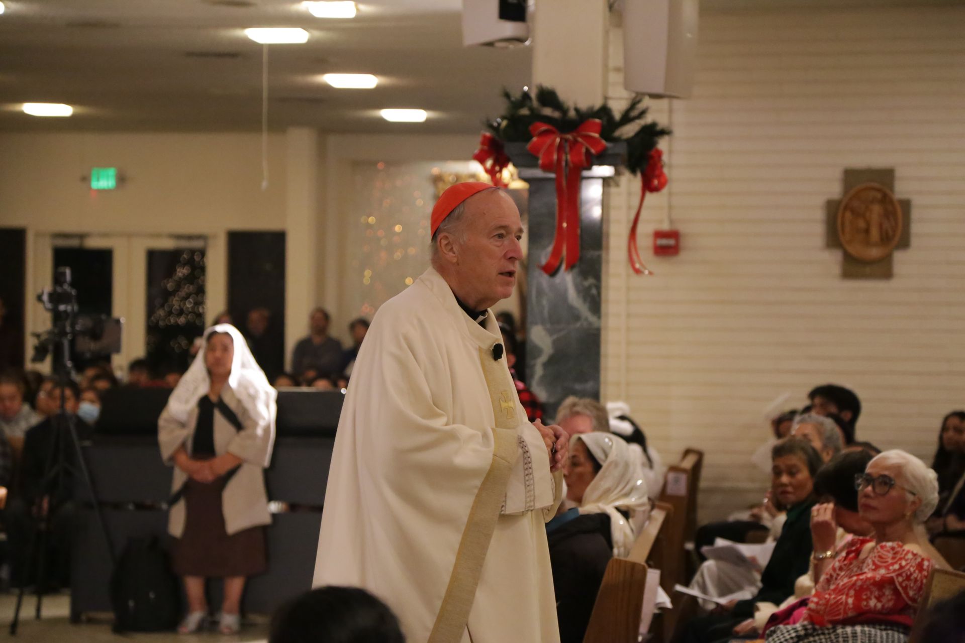 Clergy speaking in a decorated hall while seated attendees watch during a holiday gathering