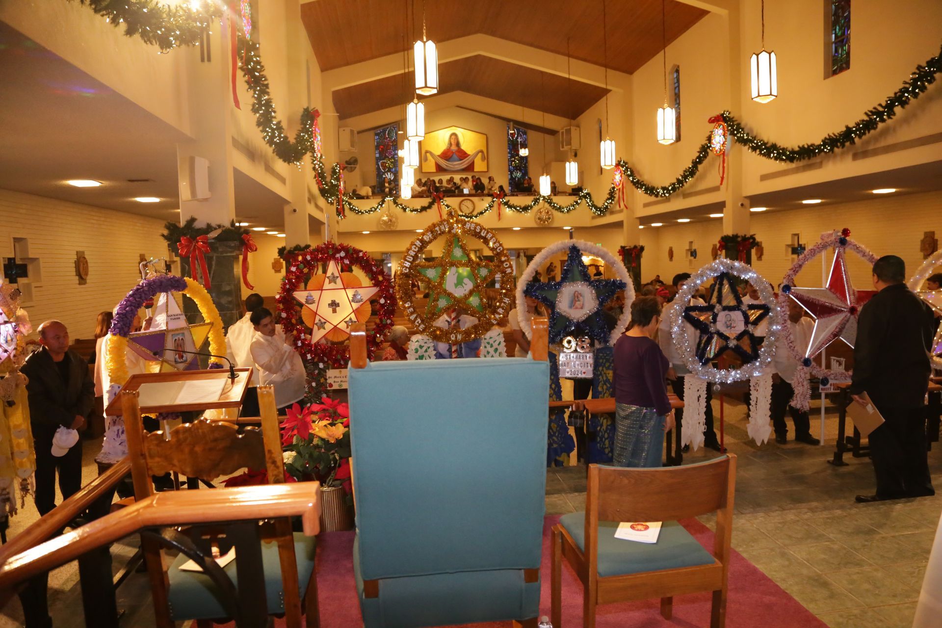 Decorated church hall with colorful holiday displays and people standing among festive wreaths and lights