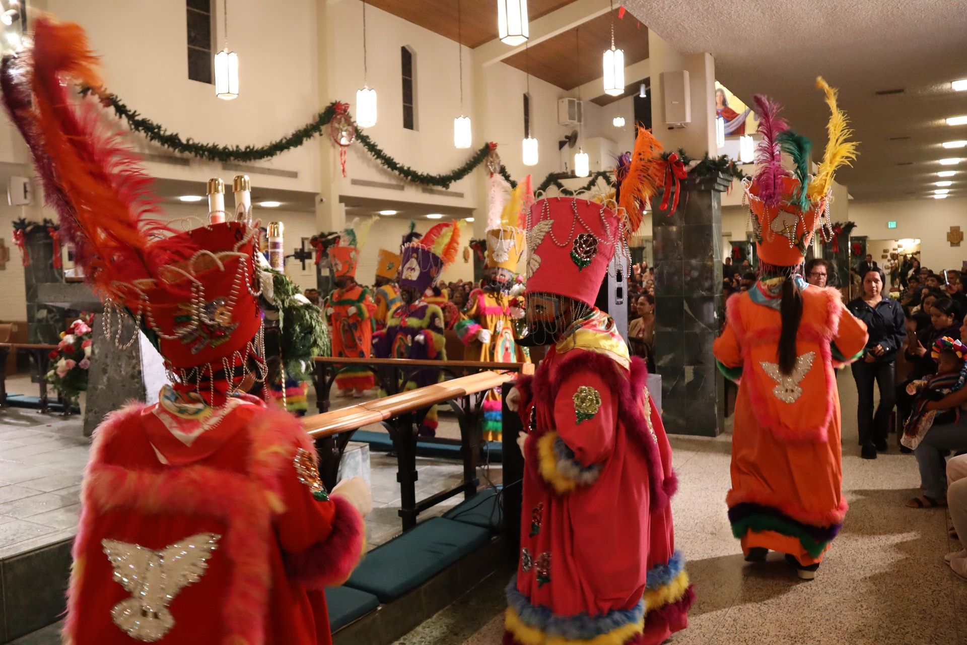 Costumed dancers in bright red and orange perform in a decorated indoor hall during a festival