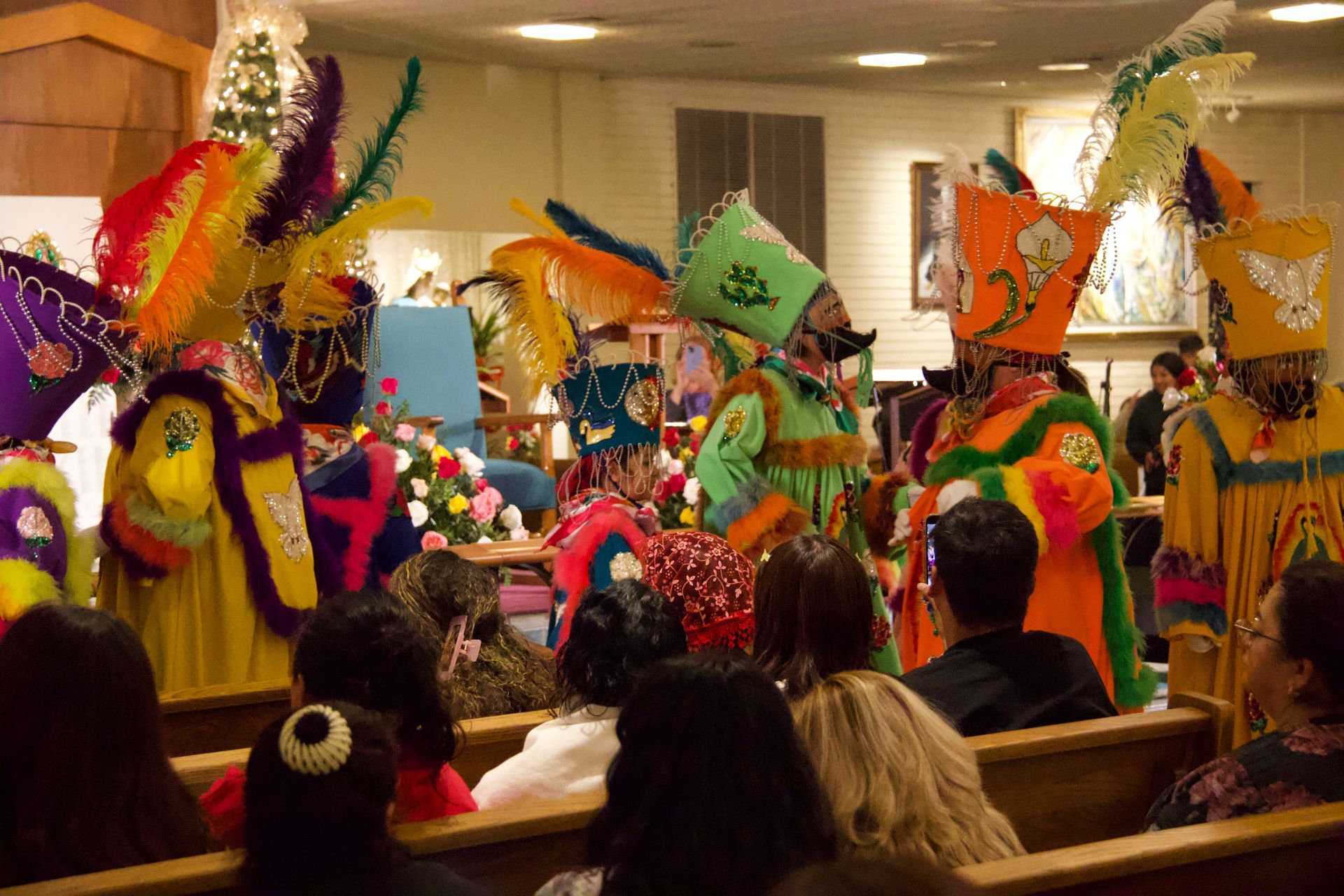 People in colorful feathered costumes performing indoors before an audience