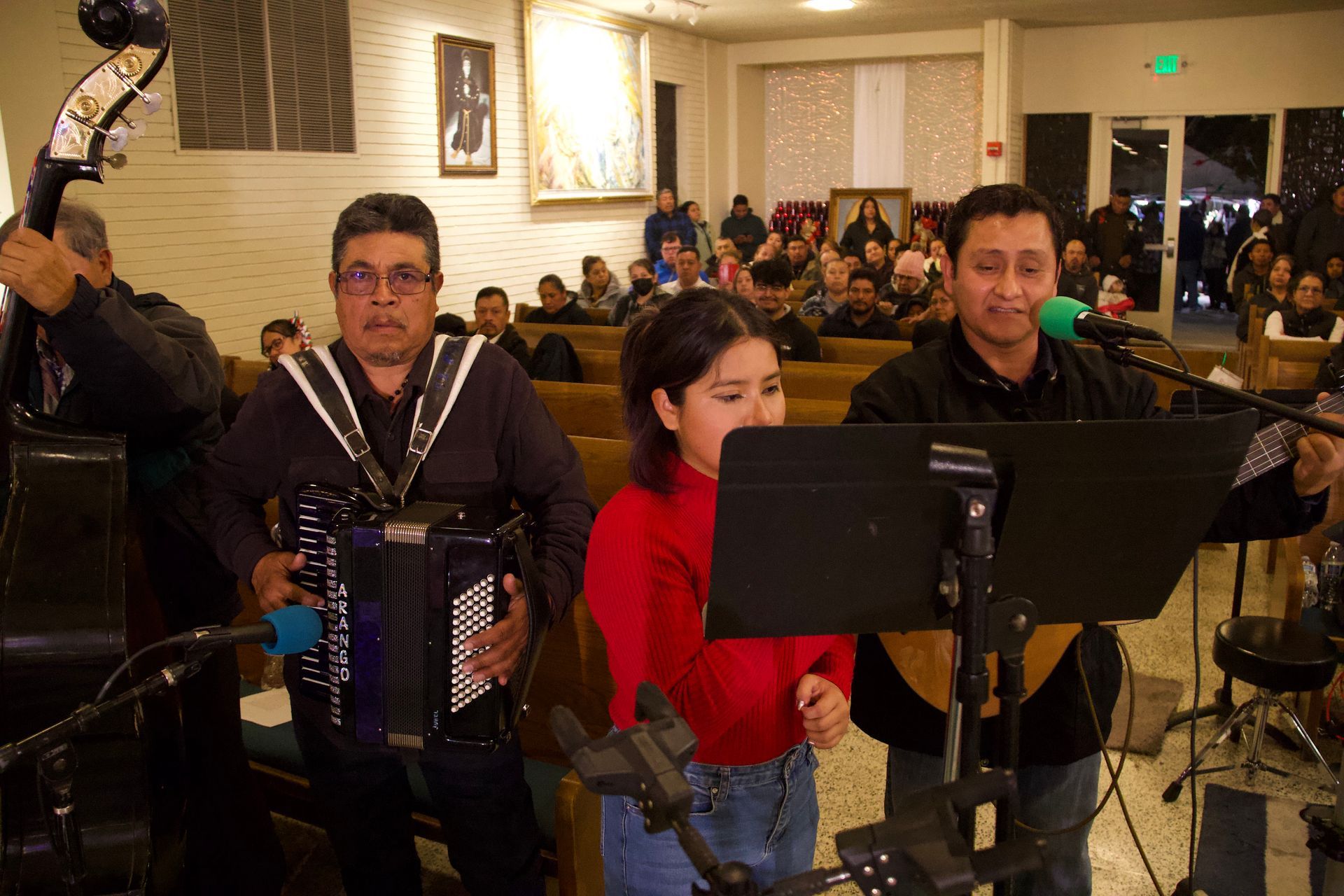 Musicians seated indoors, reading sheet music and playing accordion and guitar at a performance.