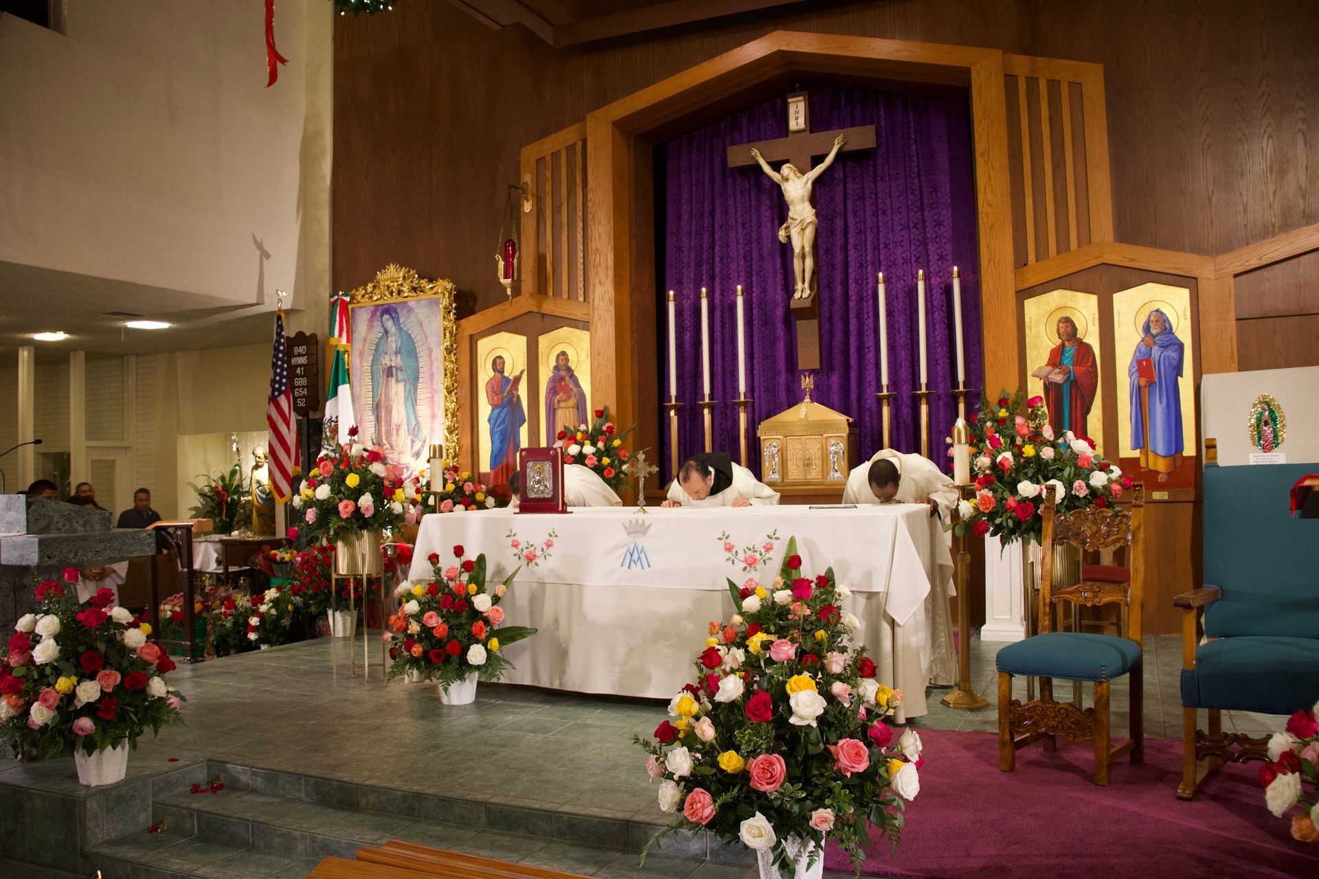 Church altar decorated with flowers and candles, with a crucifix and purple drapery behind the altar.