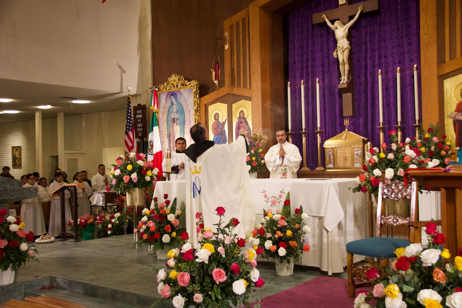 Church altar with priest, crucifix, and flower arrangements during a service