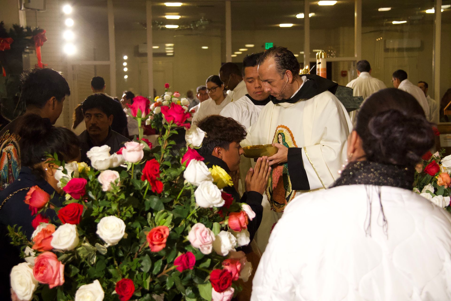 People gathered around a large bouquet of red and white flowers at an indoor ceremony.