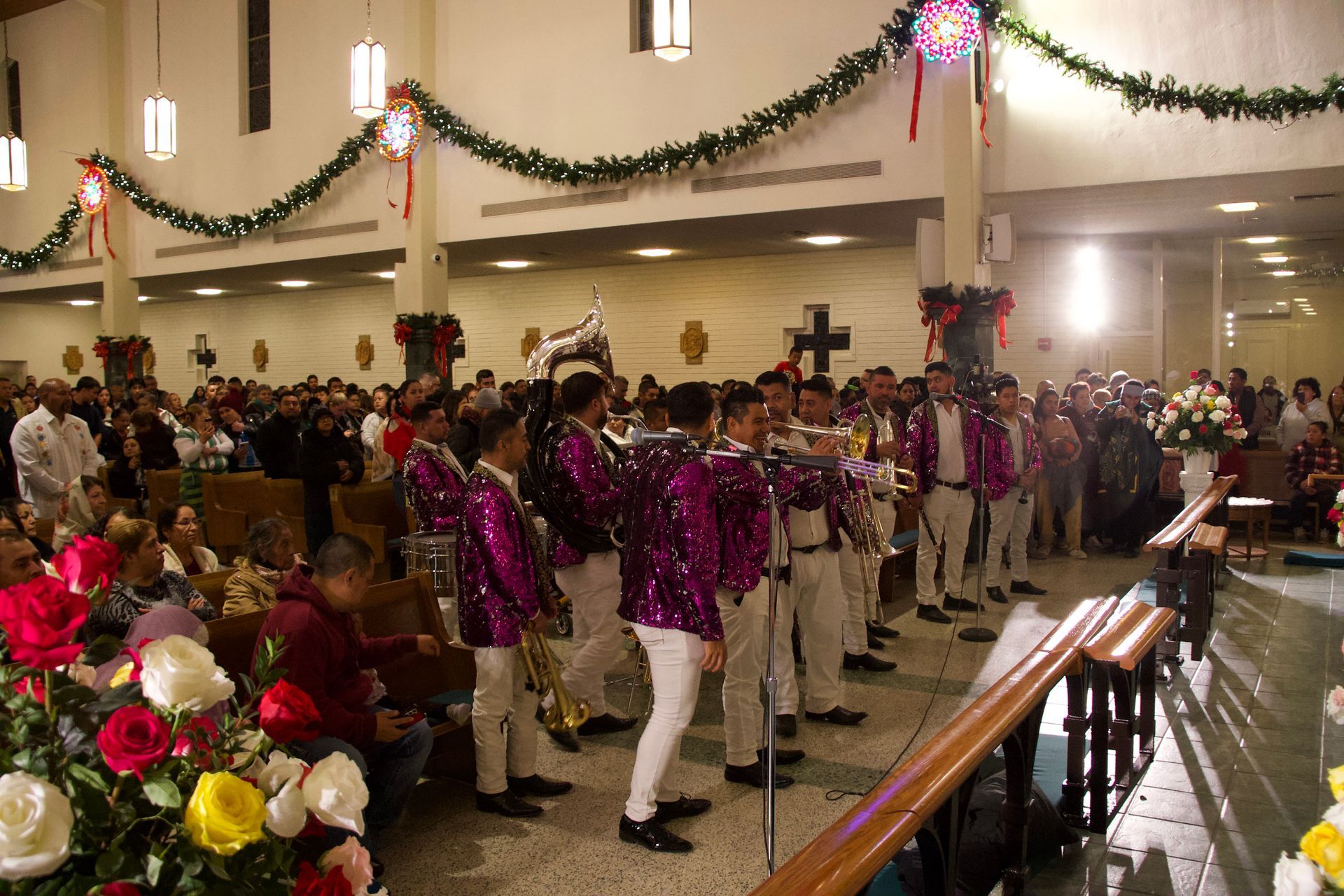 People in purple and white outfits parade through a decorated hall with garlands and flowers.
