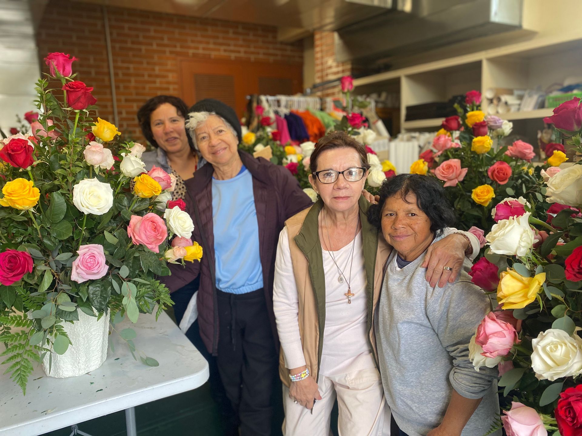 Four women posing indoors beside large bouquets of colorful flowers
