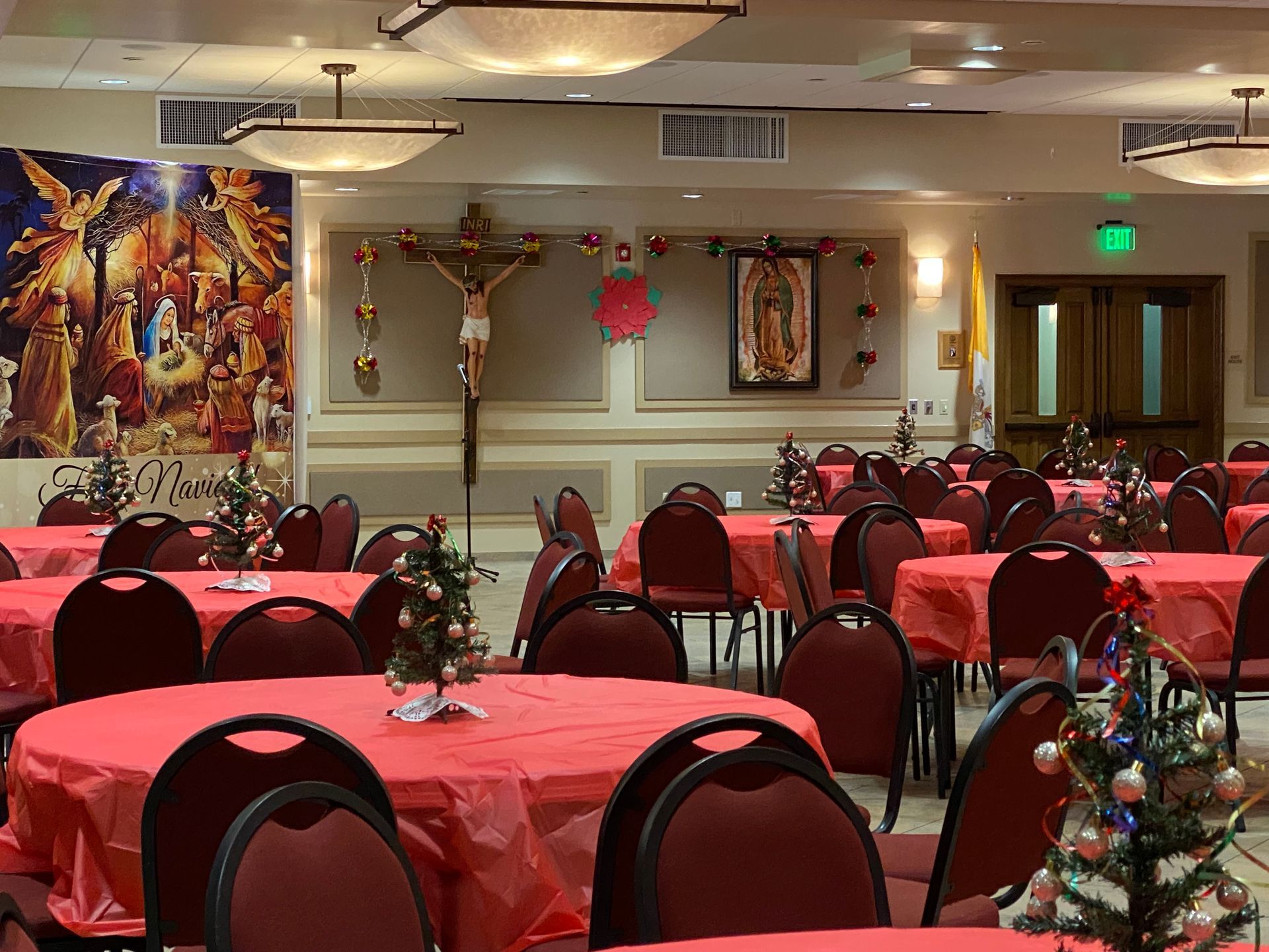 Decorated banquet hall with red tablecloths and chairs, festive wall decor, and a green exit sign