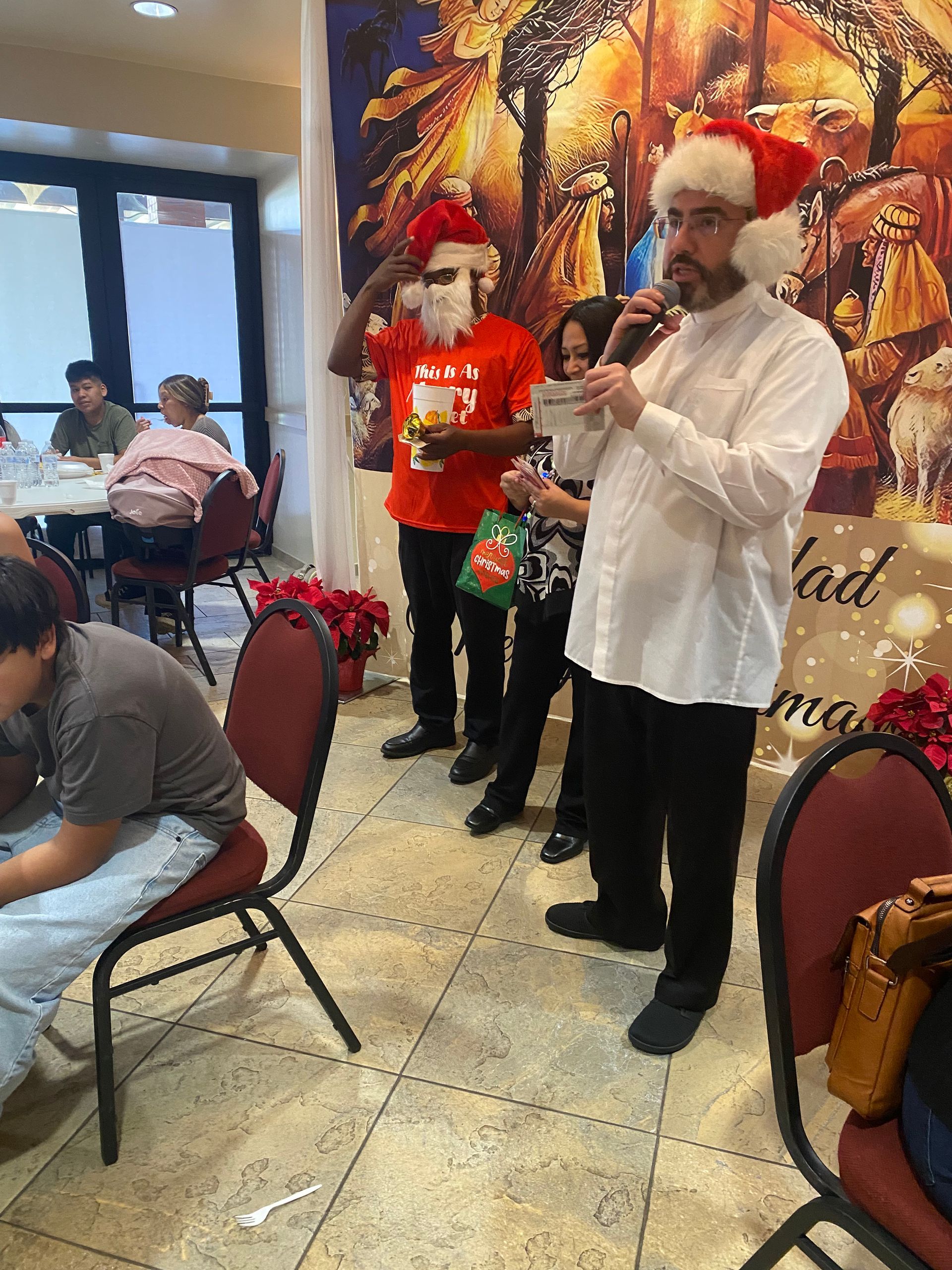 Musicians in Santa hats perform at a festive indoor event with red chairs and palm decor.