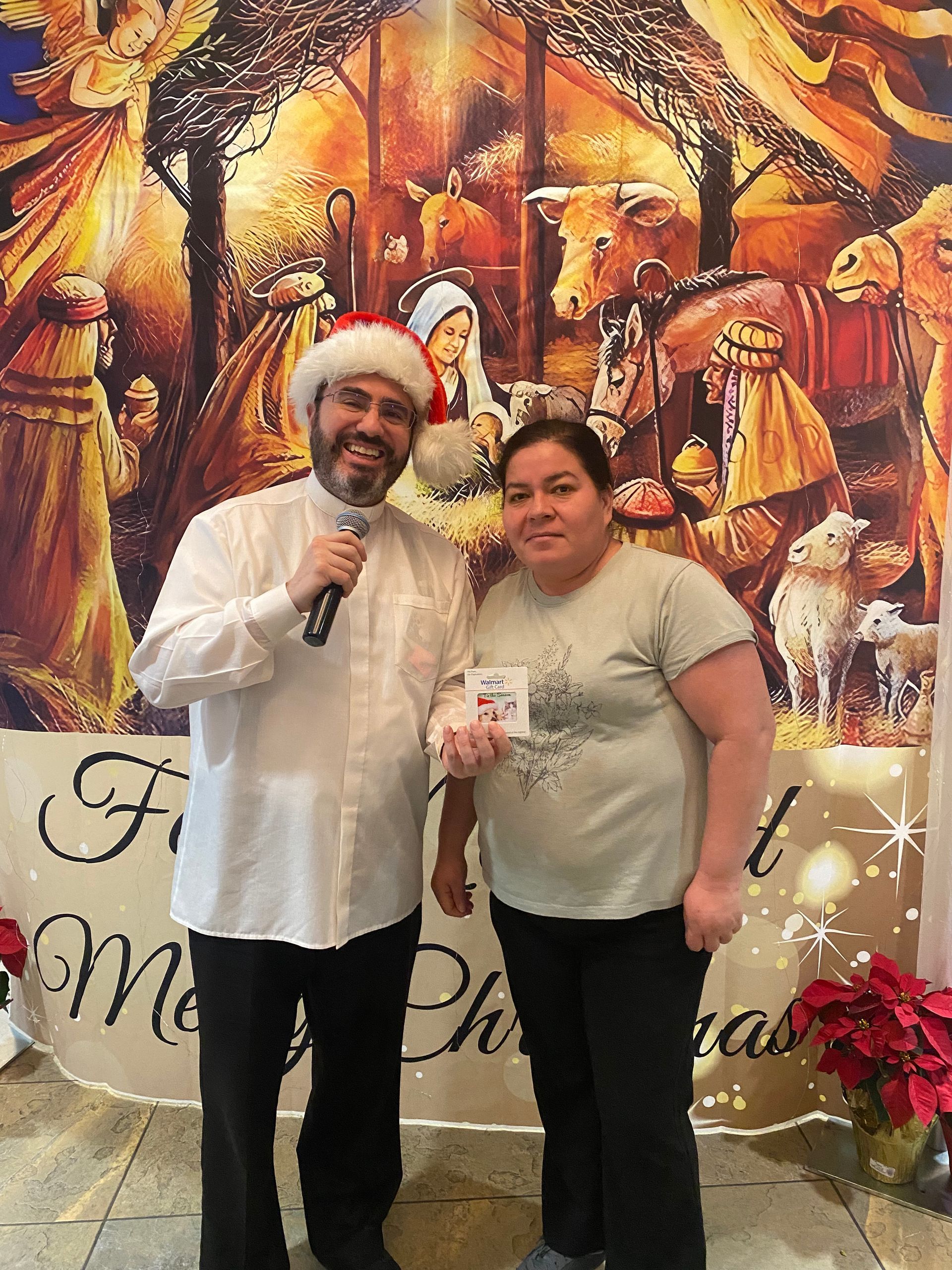 Two people posing with microphones in front of a festive Christmas backdrop.