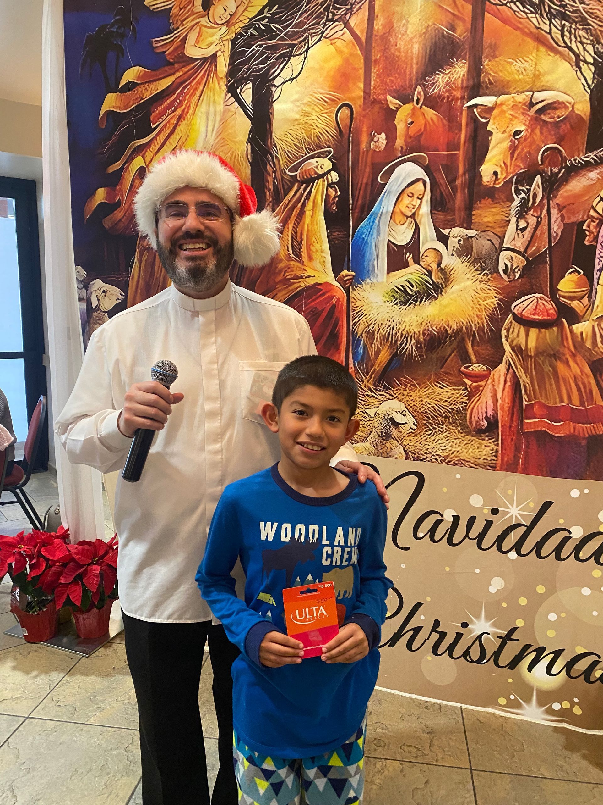 Man and boy posing with microphone and gift box in front of a colorful Christmas nativity display