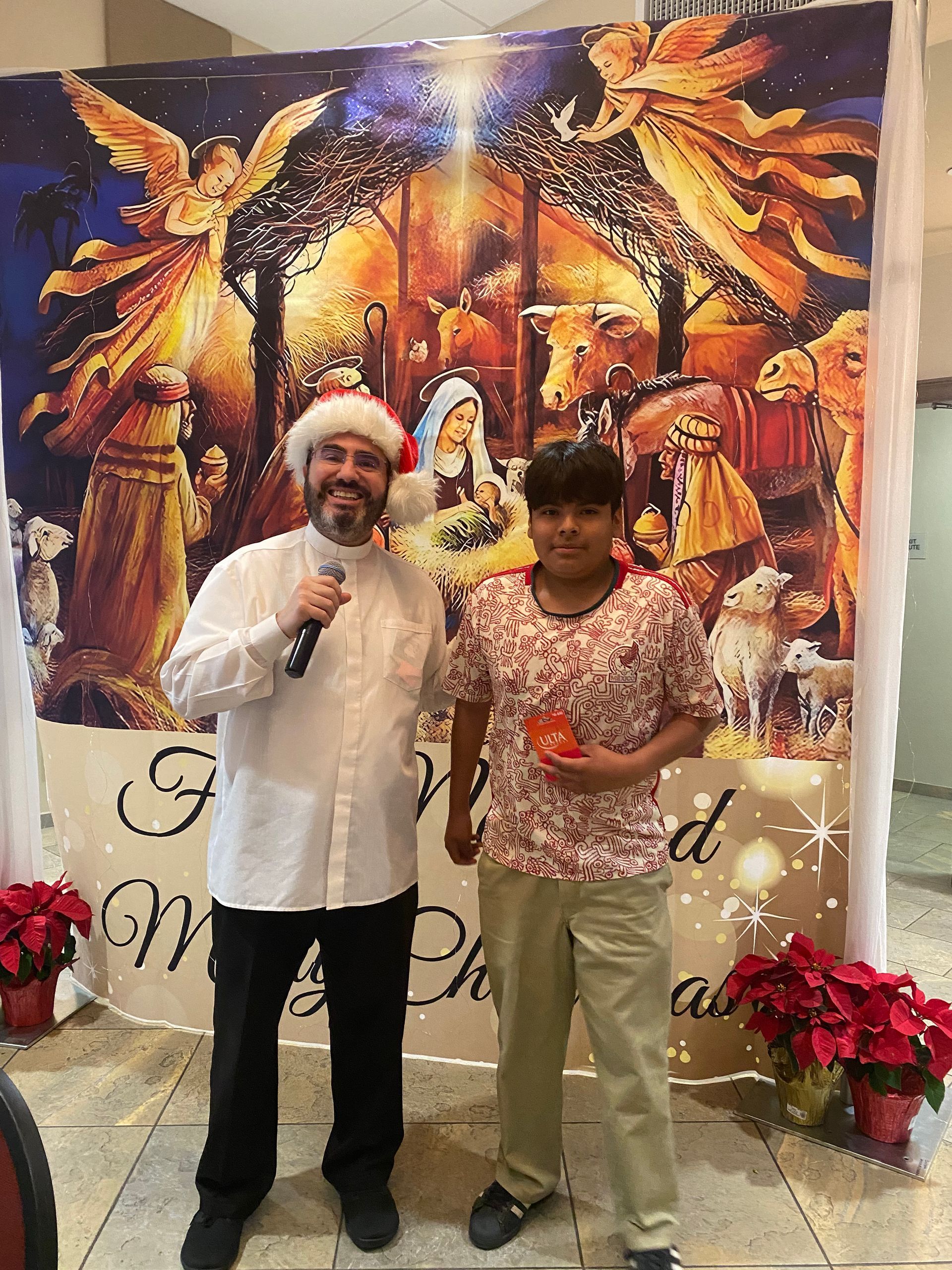 Two people standing with microphones before a festive Christmas backdrop and red poinsettias