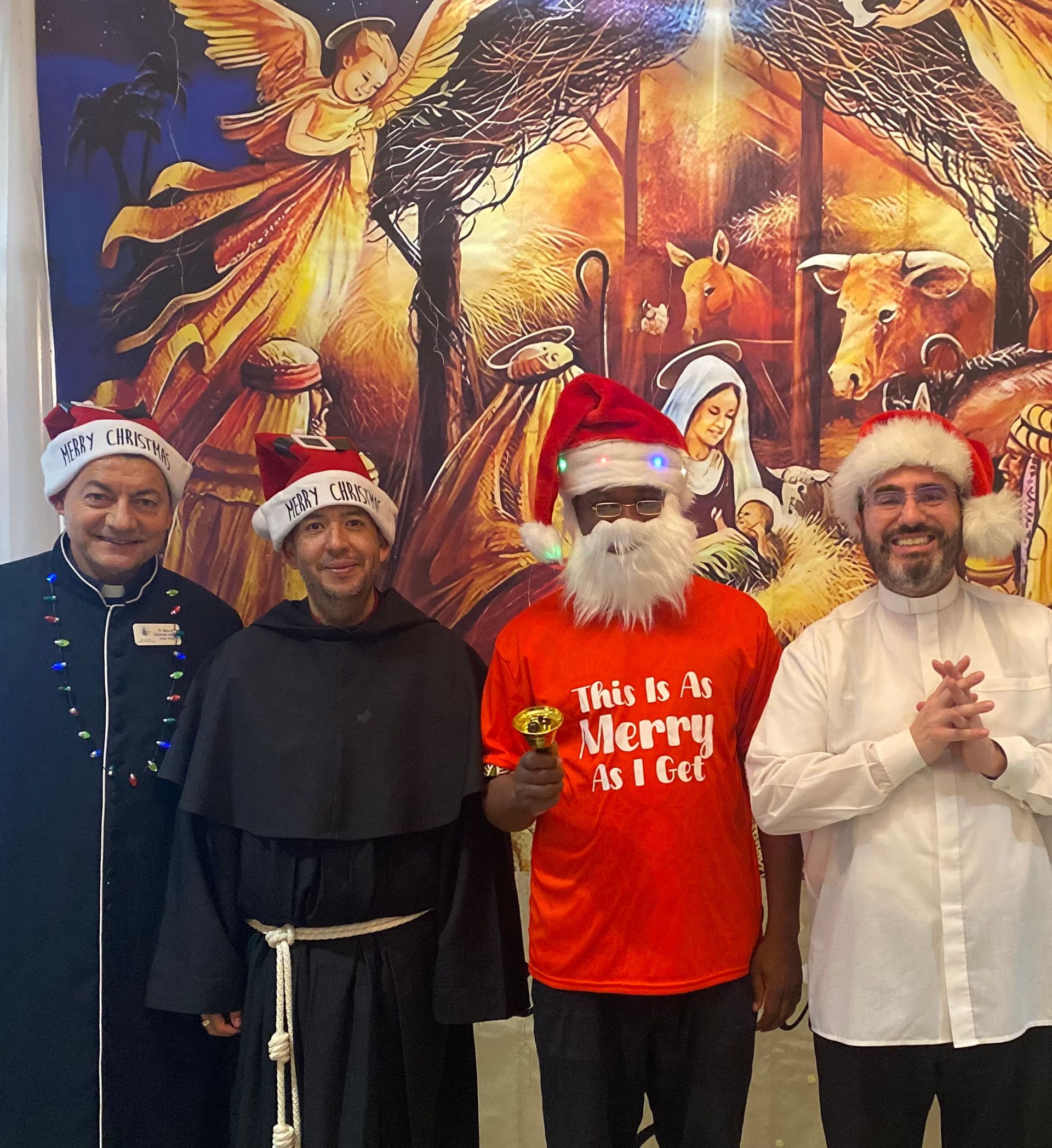 Four people in Santa hats pose in front of a festive holiday mural.