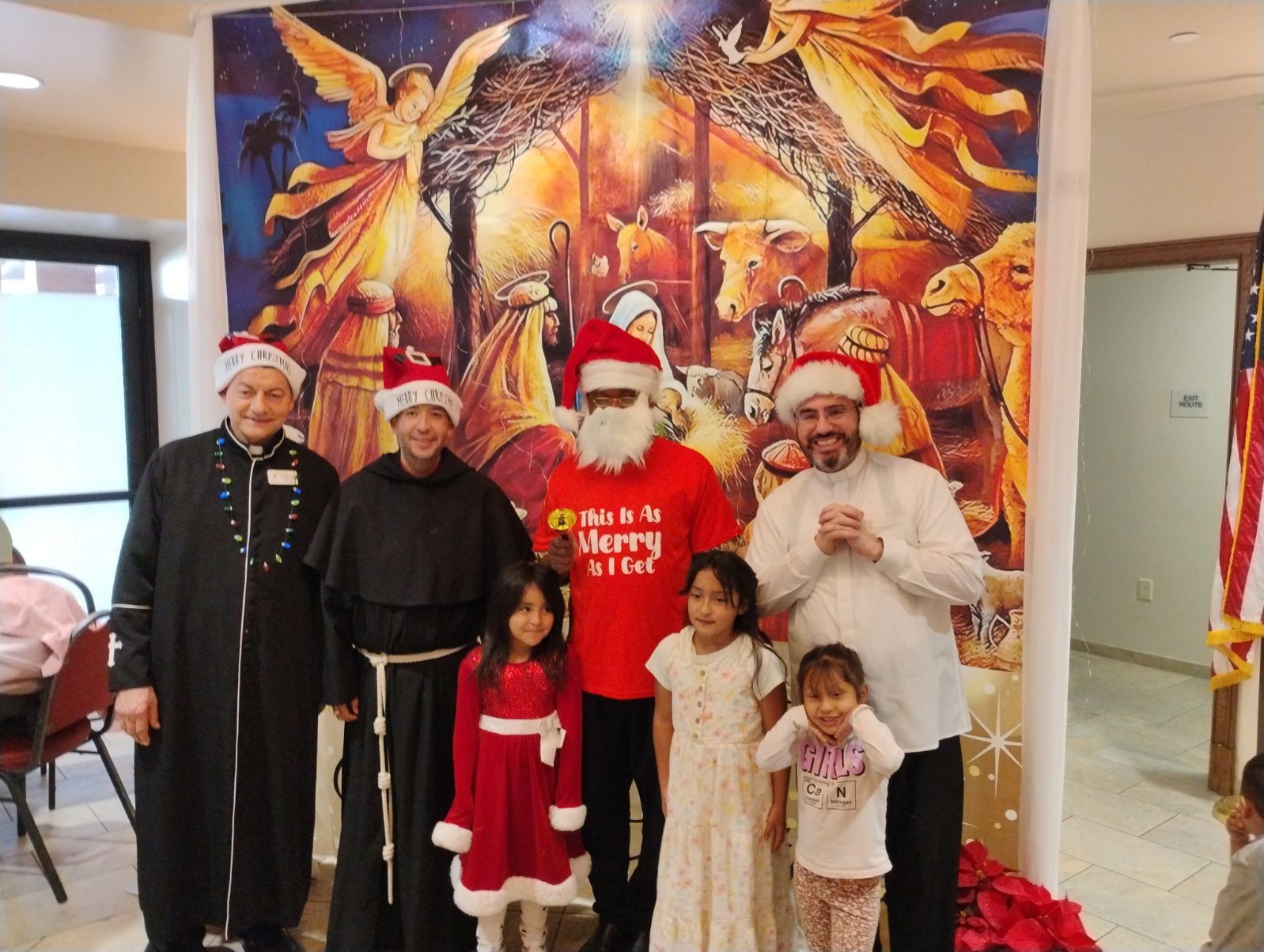 Group in Santa outfits posing indoors in front of a colorful holiday mural.
