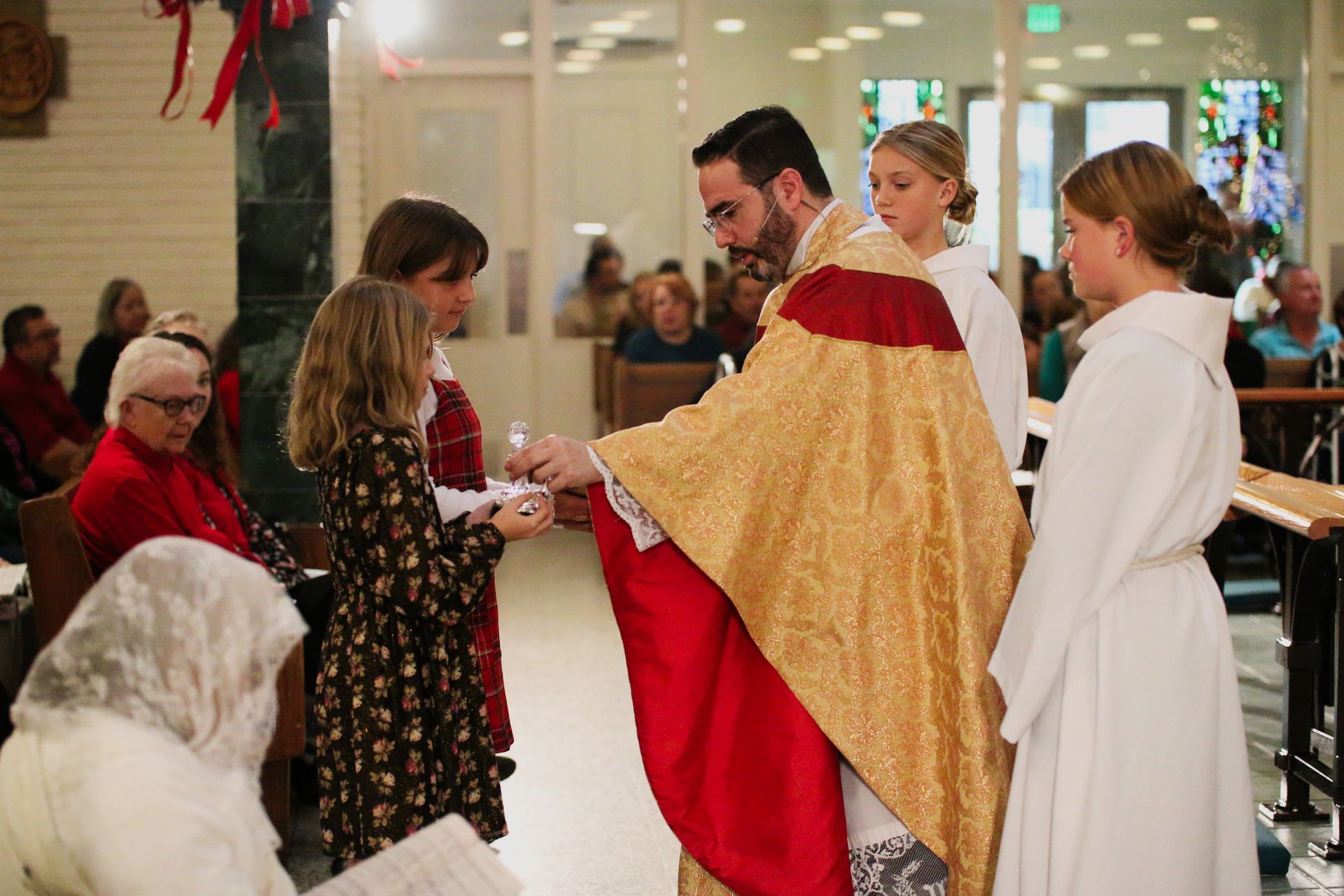 People in church exchanging communion, with a priest in red and gold vestments handing bread to attendees.