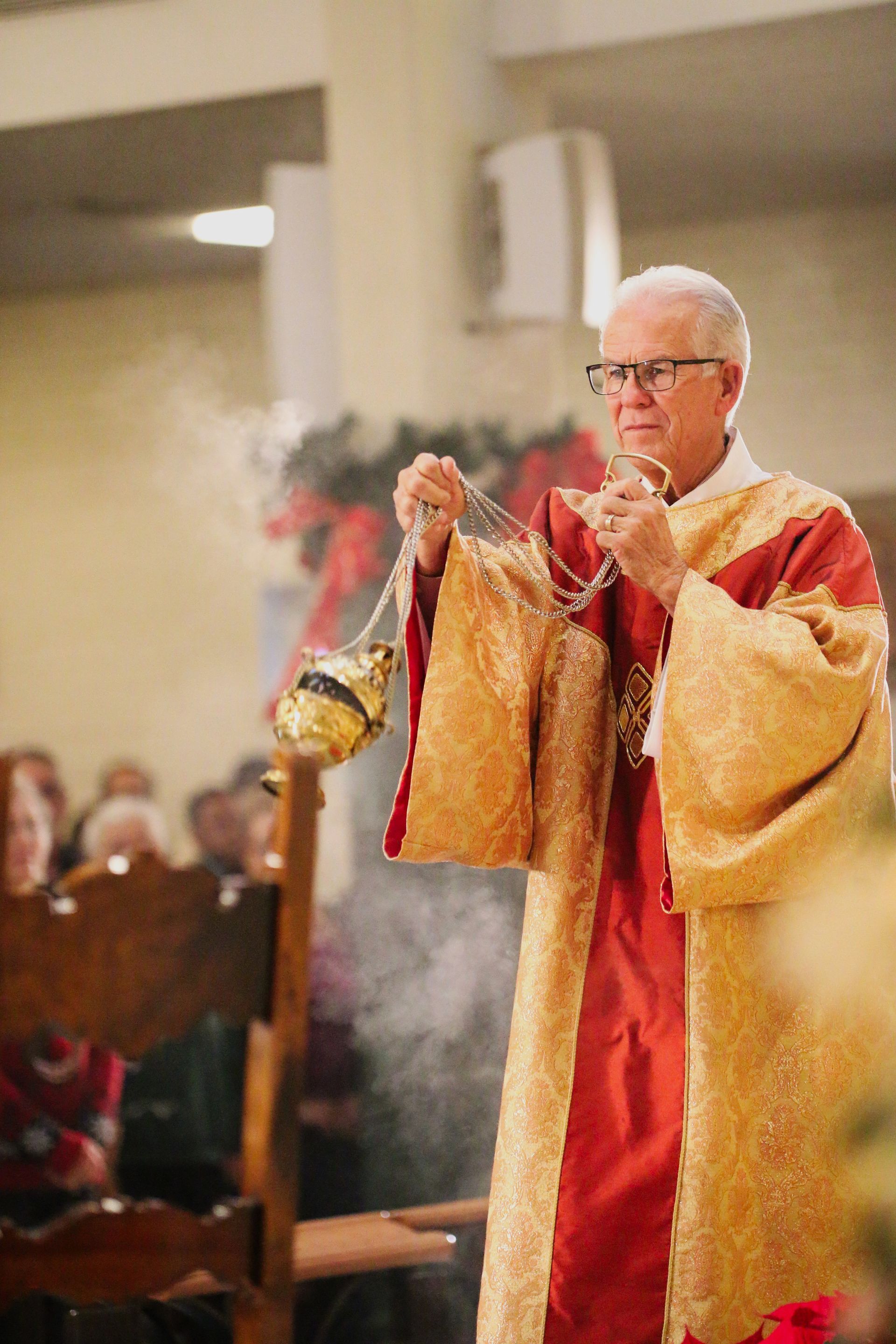 Priest in red and gold vestments holding a censer during a church ceremony