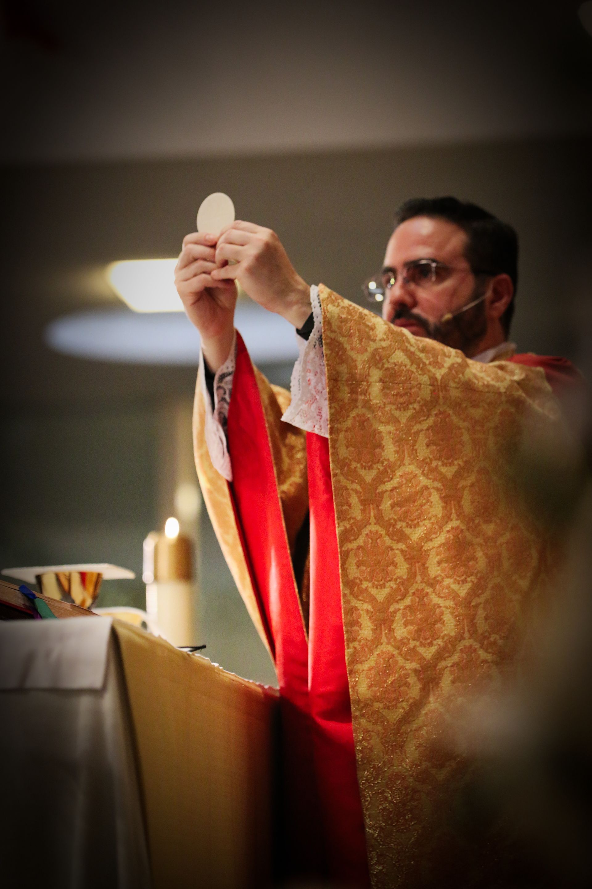 Priest in gold vestments lifts a red cloth during a church ceremony at the altar