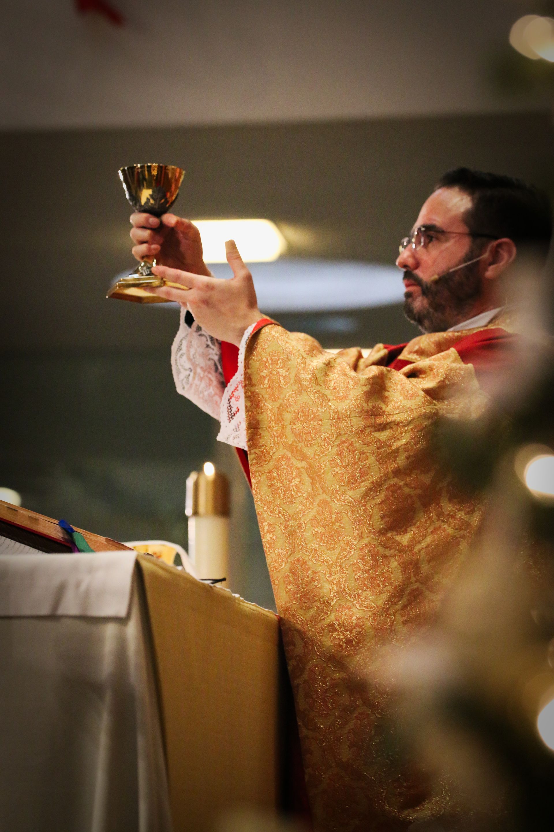 Priest in gold vestments raising a chalice during a church ceremony
