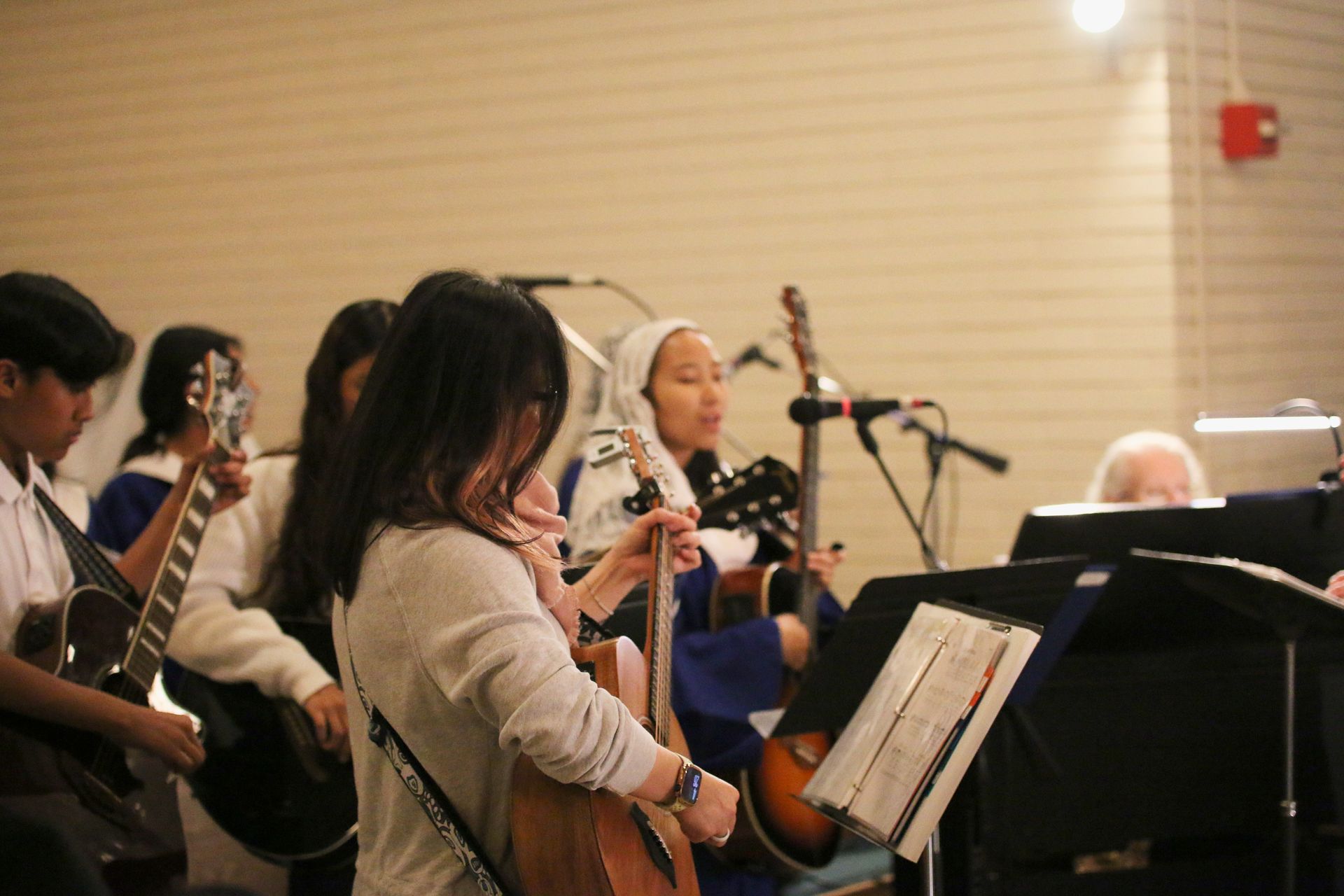 Musicians rehearsing with violins and microphones in a hall, with sheet music stands in front.