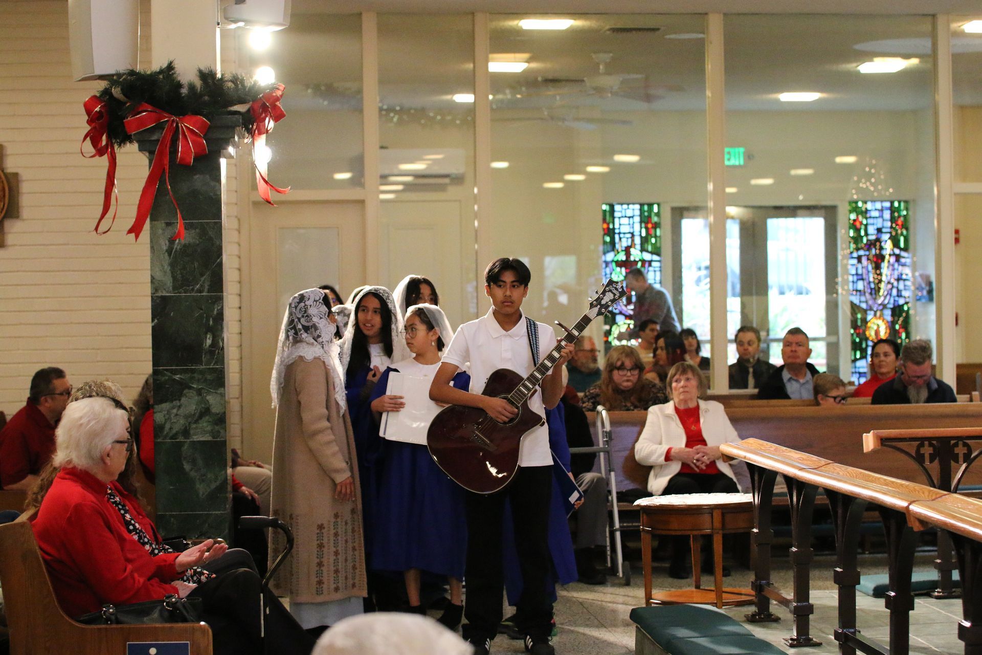 People standing and singing with a guitar in a decorated indoor church or hall hallway