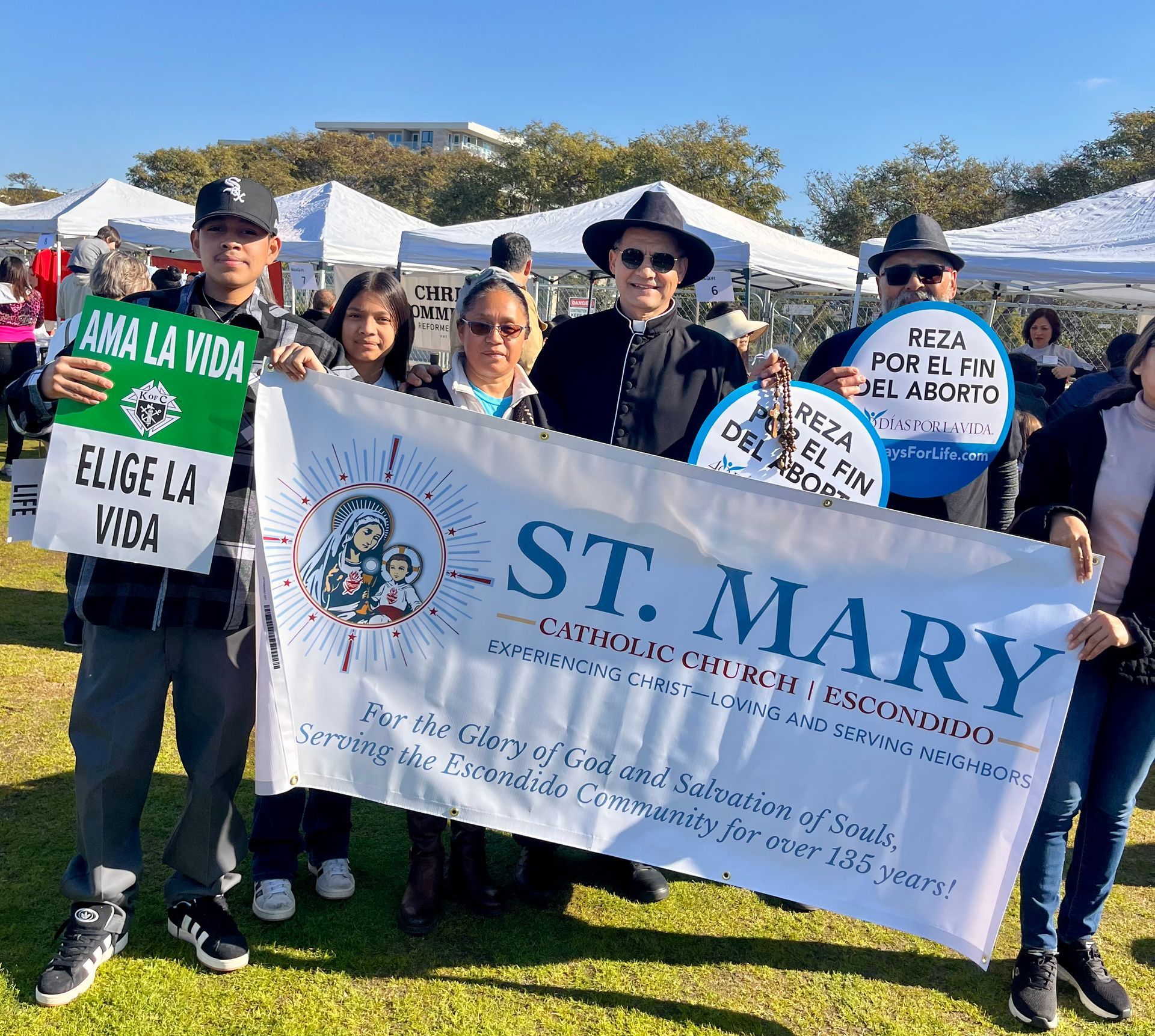 People holding banners at a St. Mary pro-life event outdoors in bright sunlight