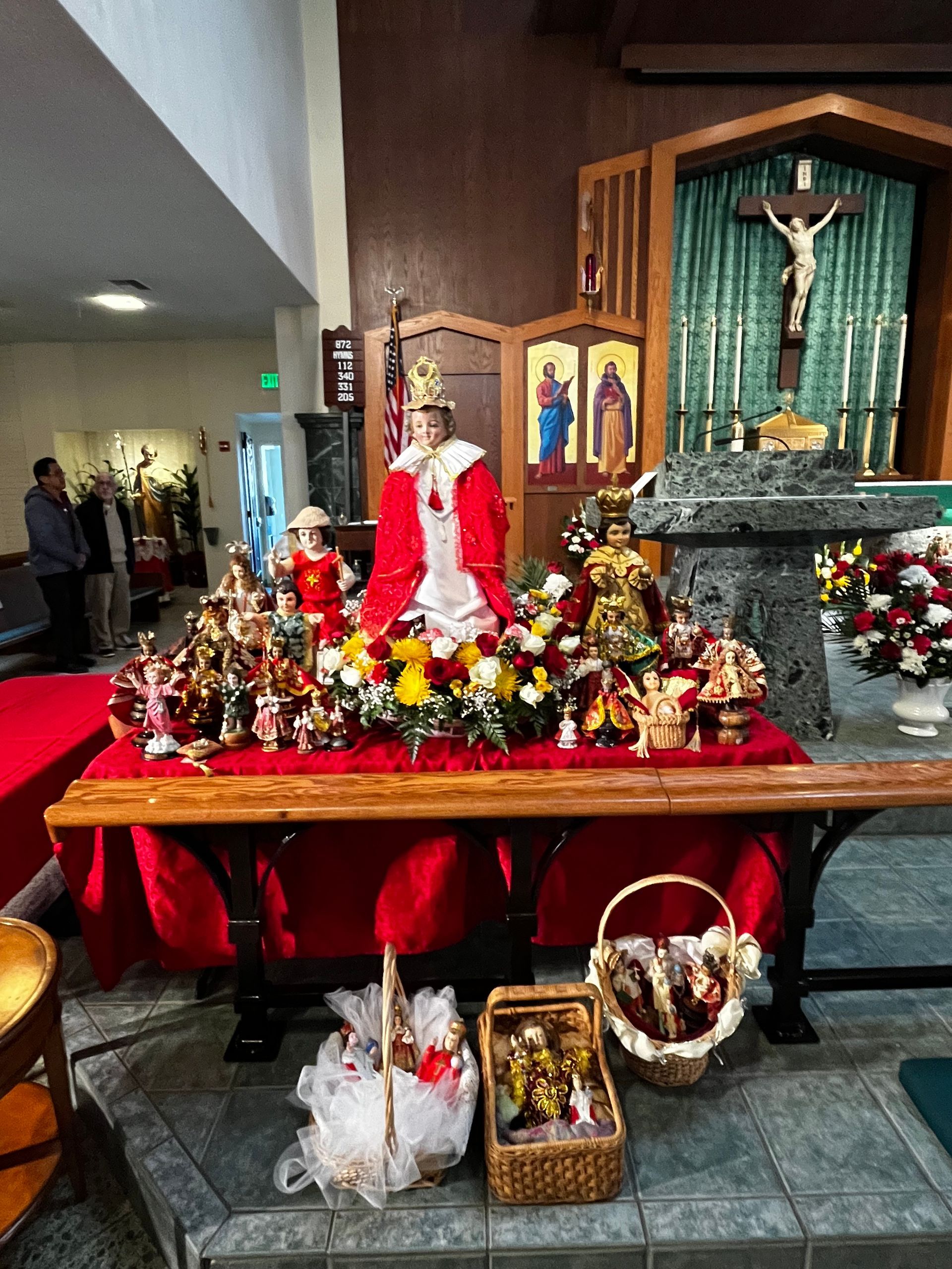 Decorated church altar with a nativity scene, red cloth, flowers, and a crucifix in the background