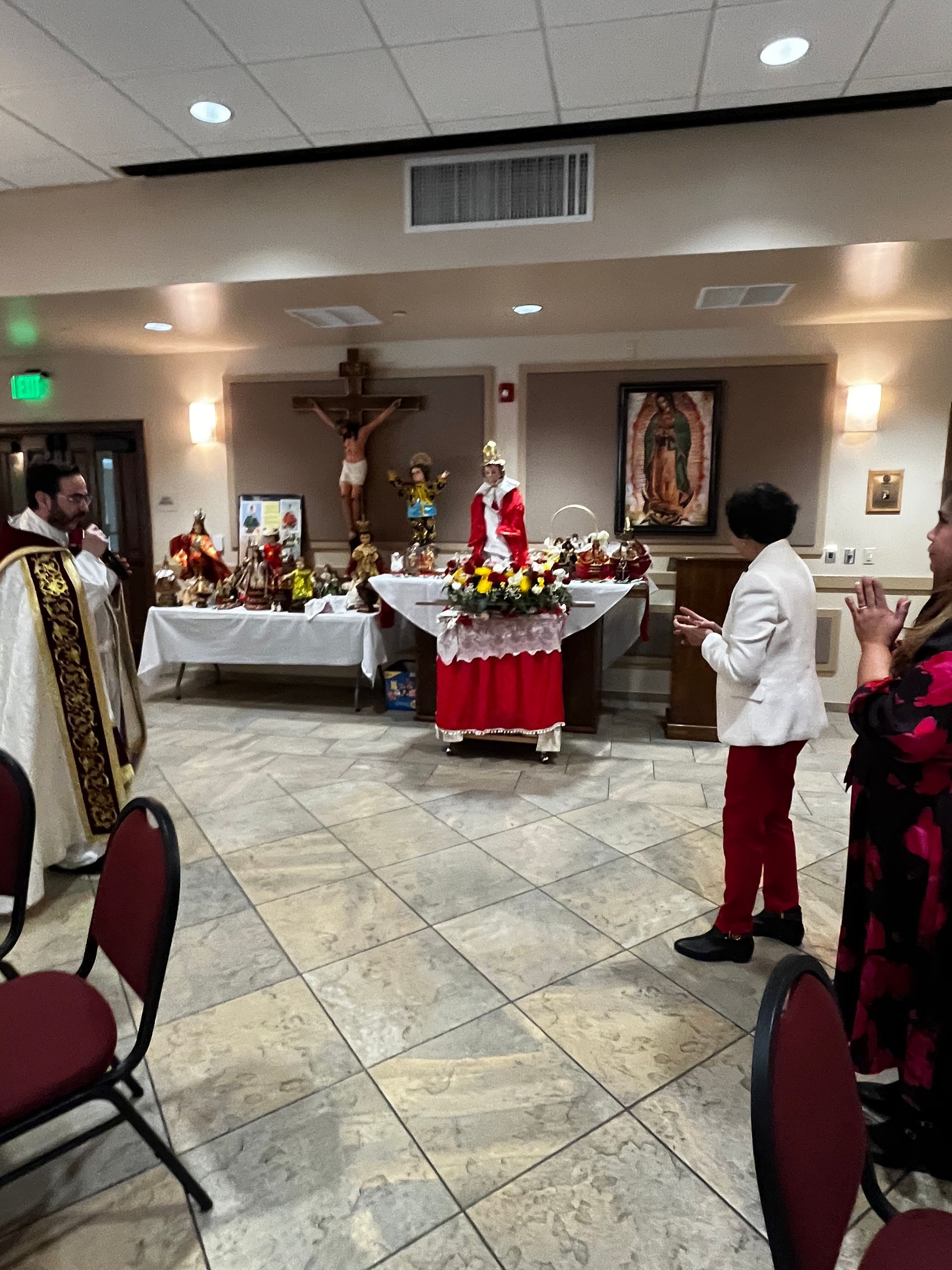 Church altar decorated with flowers, candles, and a crucifix, with people standing nearby in a hall